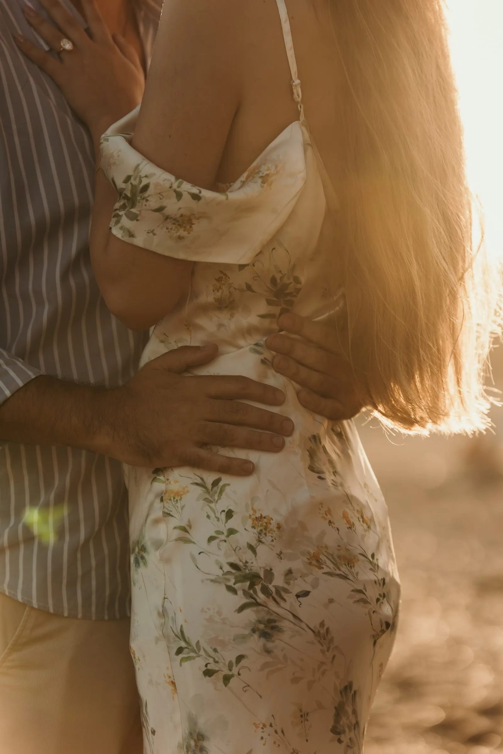 Close-up of his hands on her waist and her long hair in golden backlight, beach in Nerja