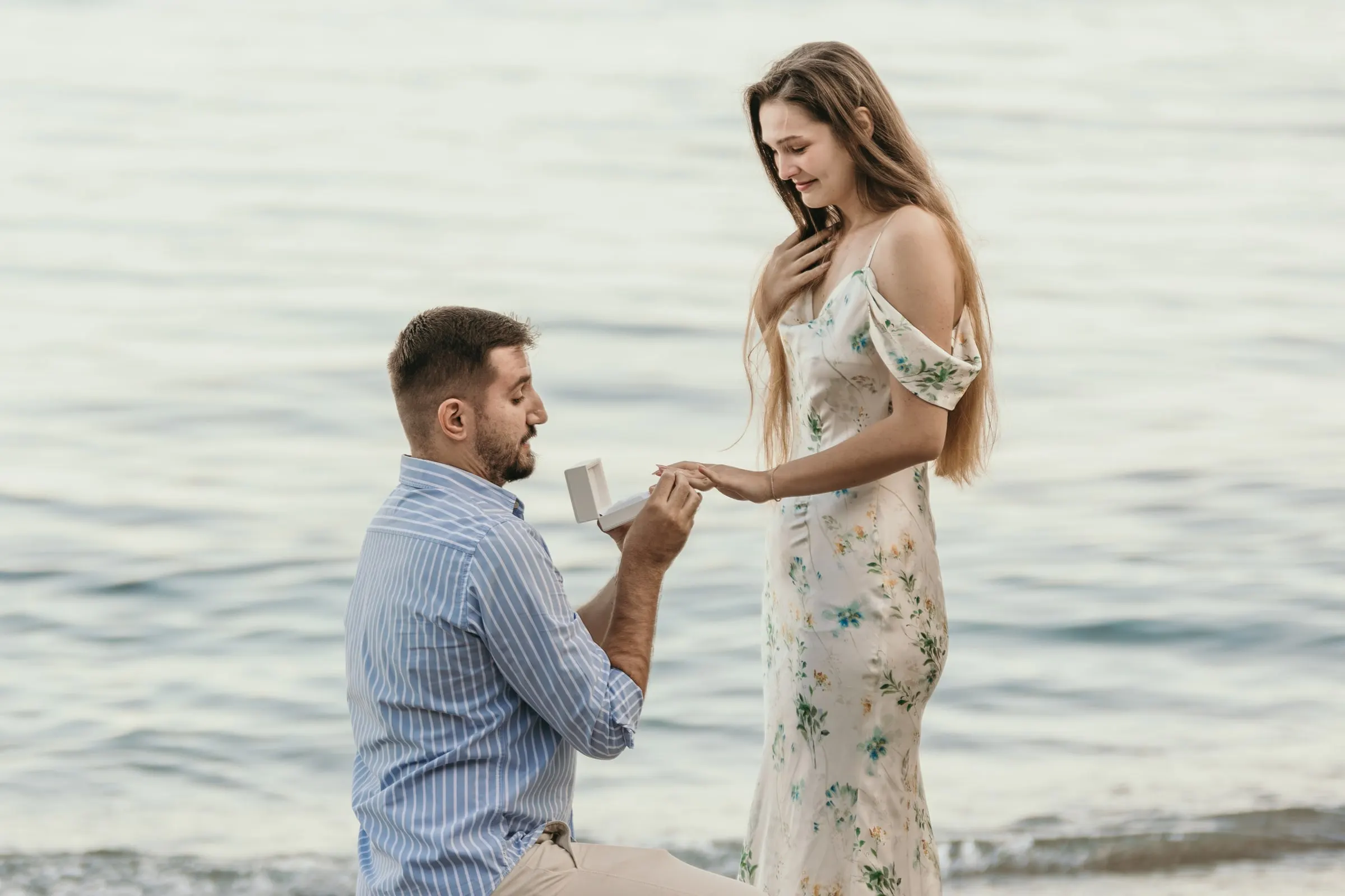 He slips the ring on her finger, kneeling at the water's edge, on the beach in Nerja