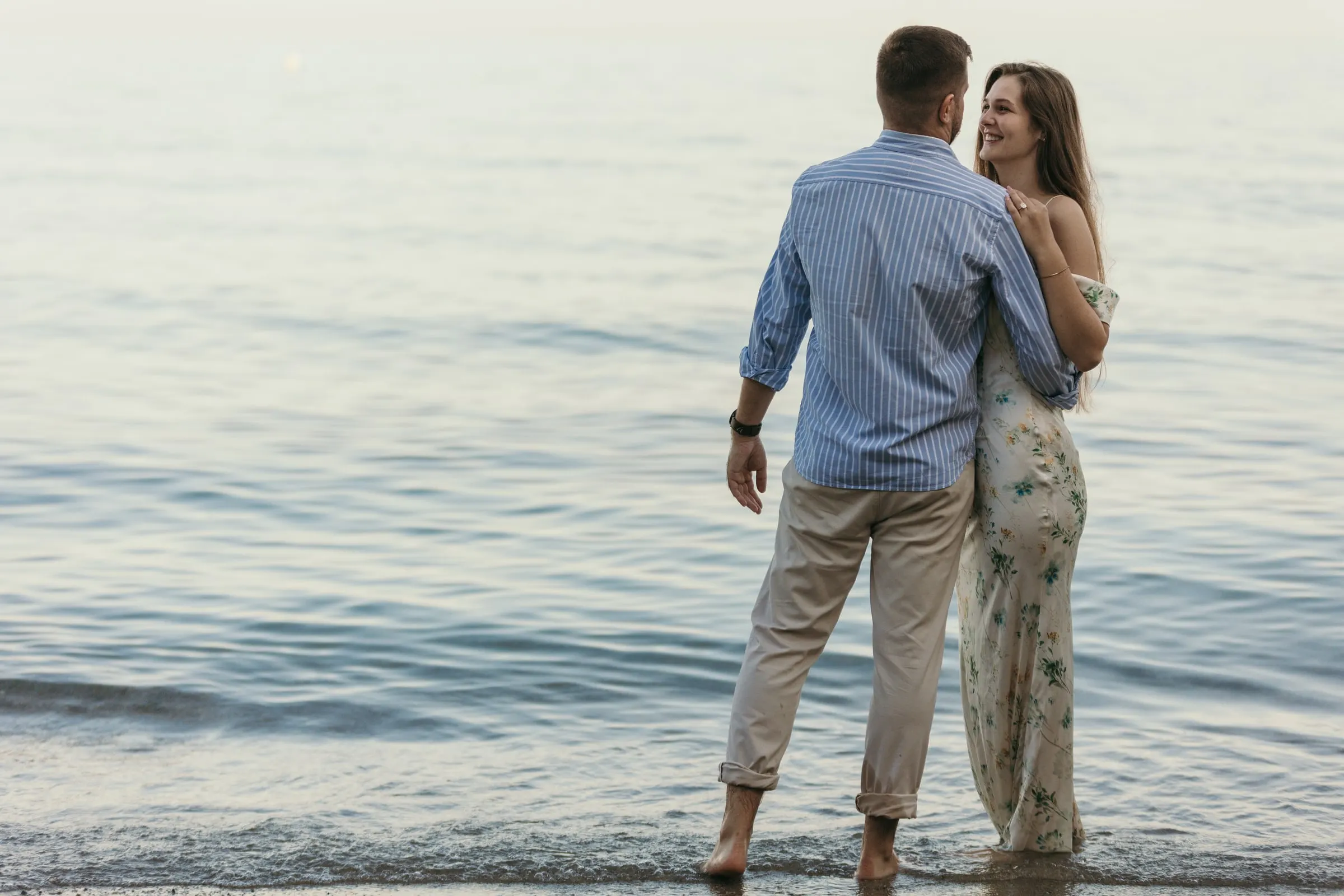 Couple standing in the shallows as she looks back and smiles, on the beach in Nerja