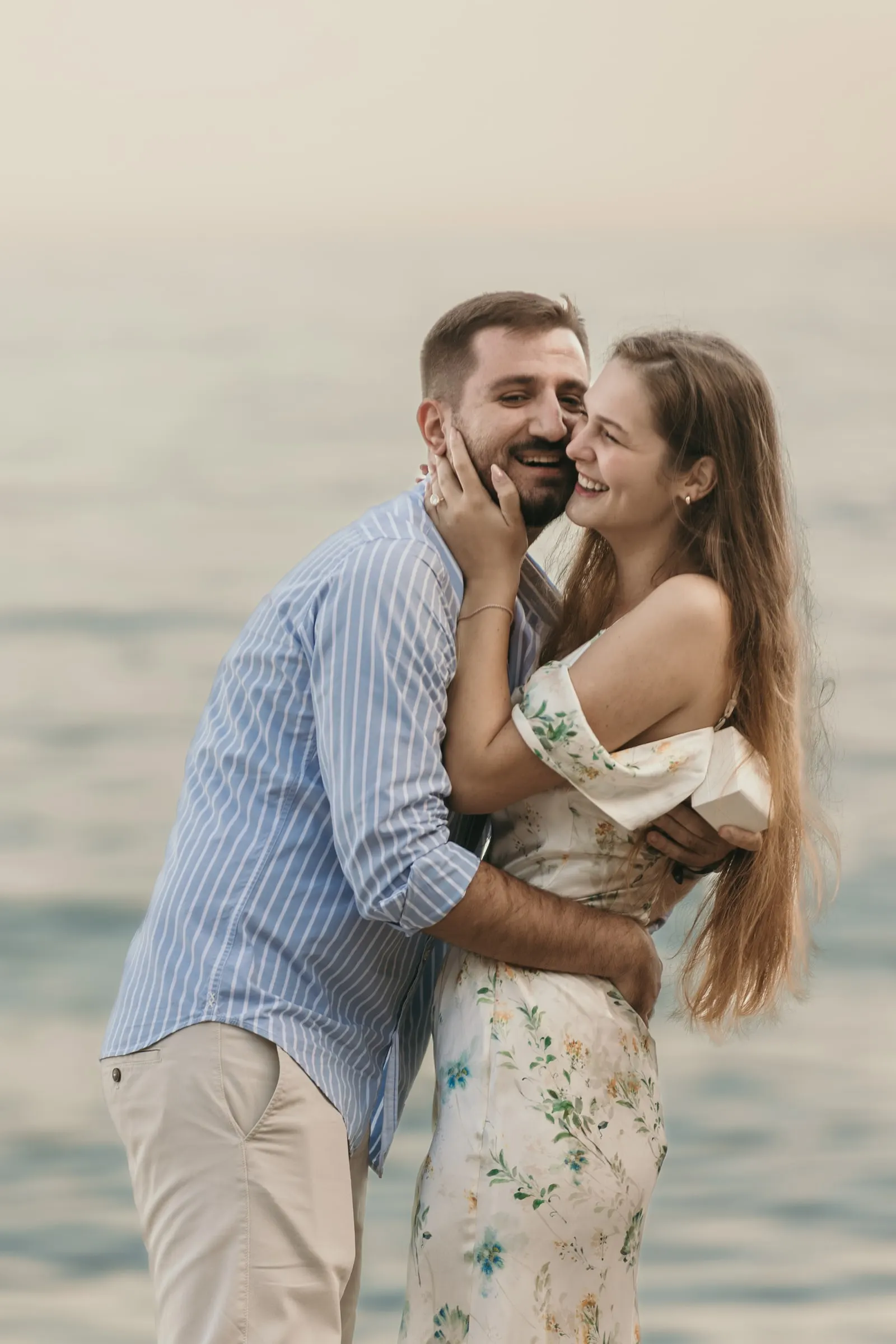 He holds her face as they hug and laugh by the water, on the beach in Nerja
