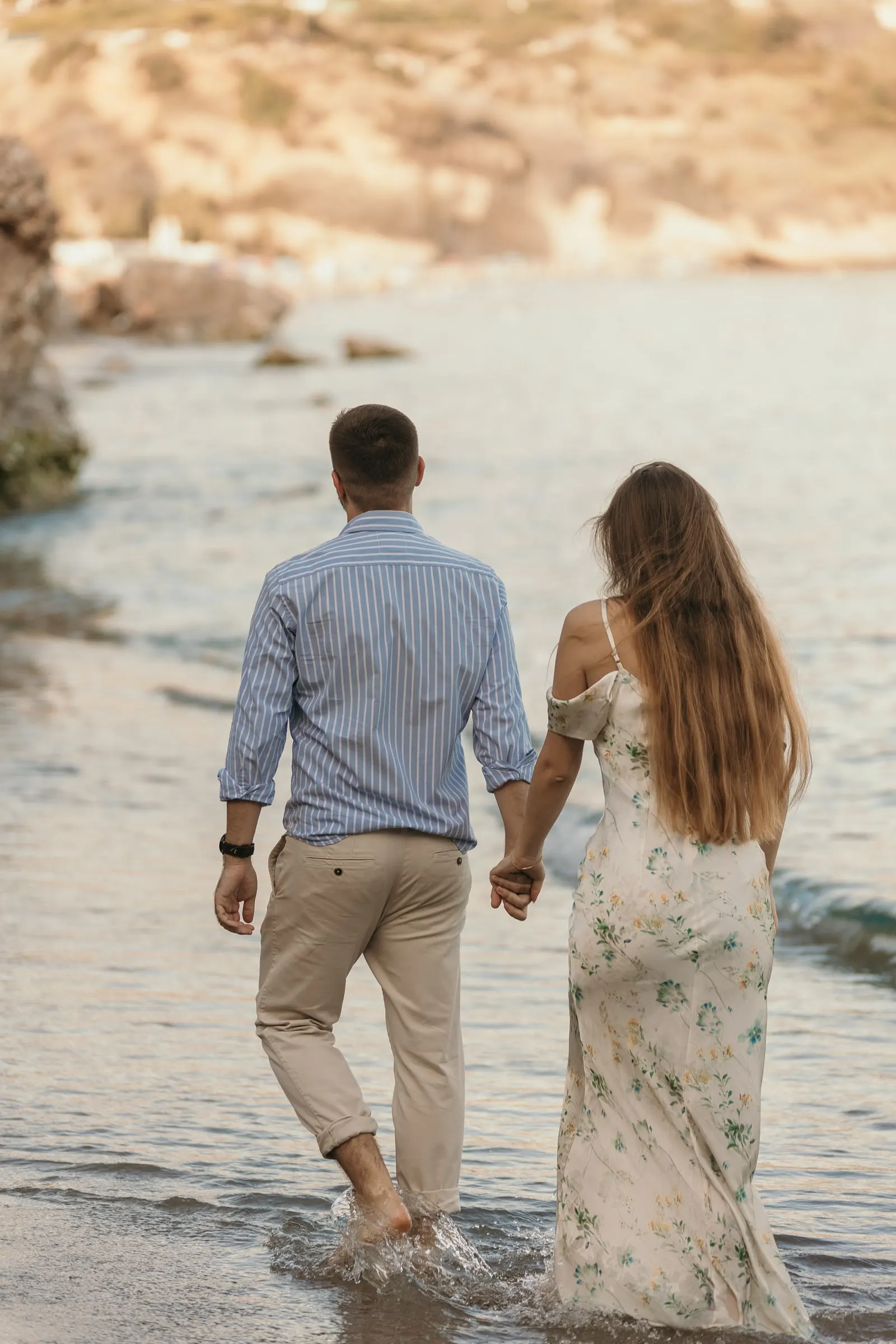 Couple walking hand in hand through the shallows towards the cliffs, on the beach in Nerja