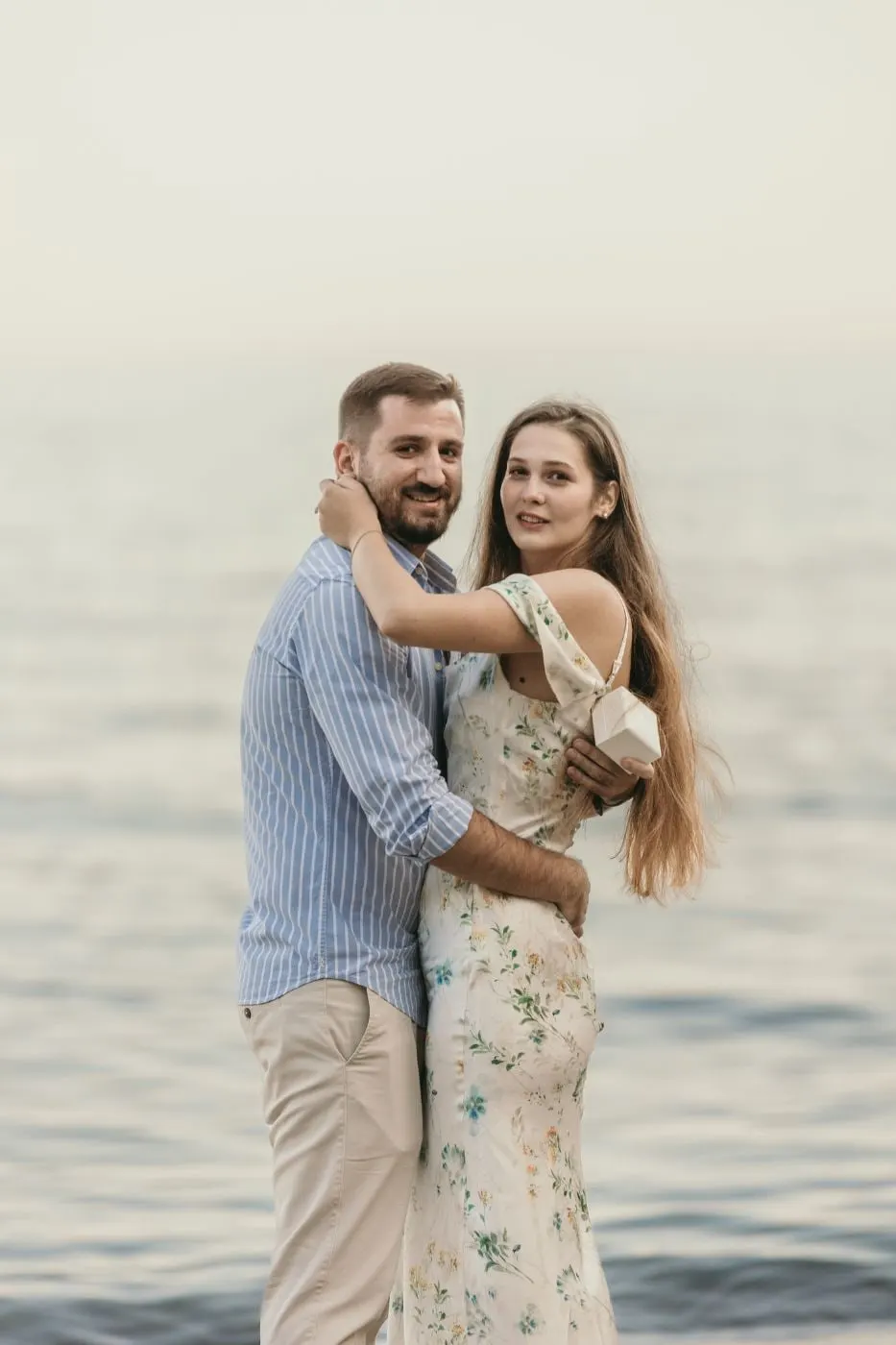 Couple hugging and looking at the camera with the calm sea behind, on the beach in Nerja