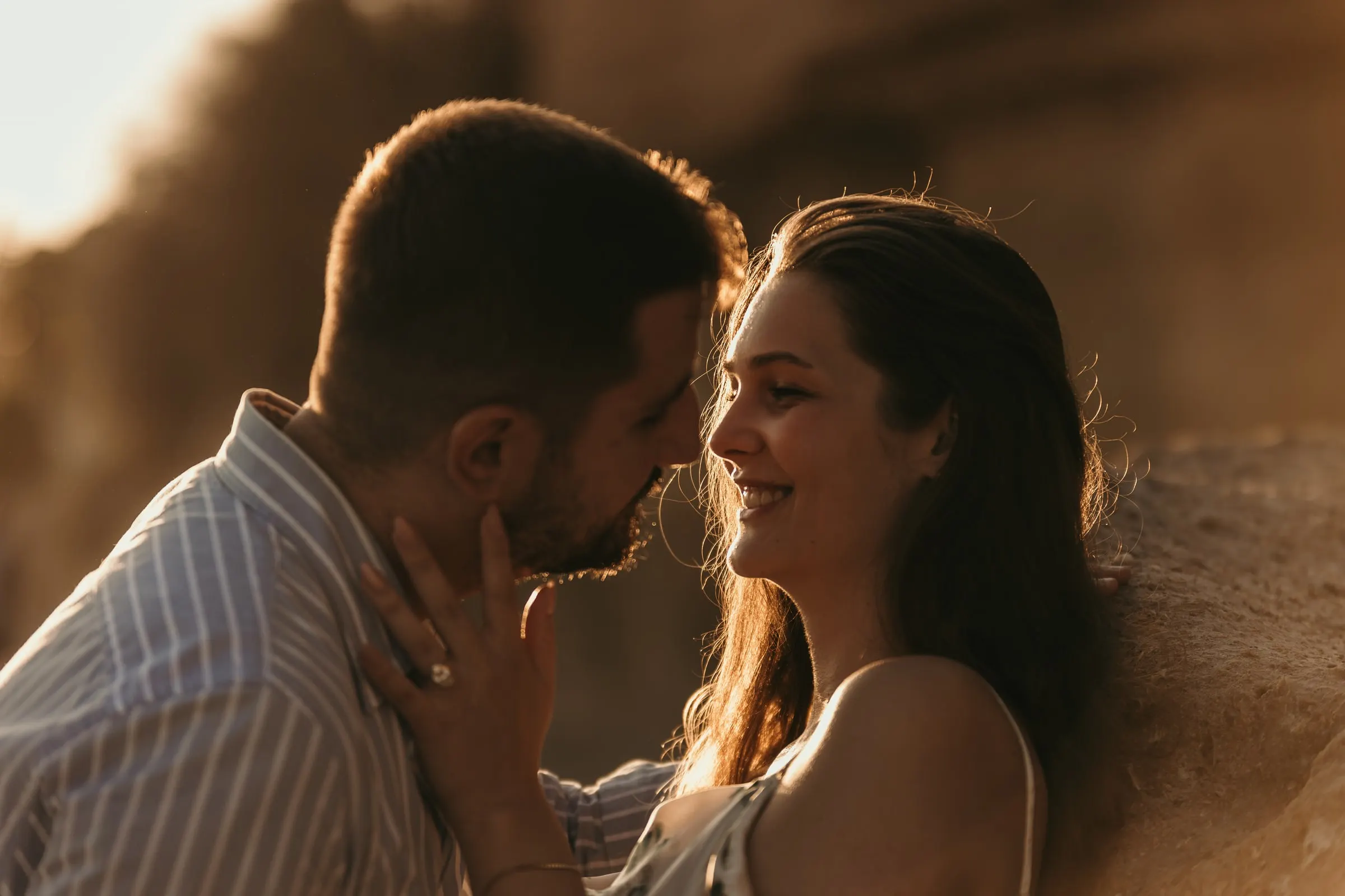 He kisses her cheek as she holds his face, the ring in view, on the beach in Nerja