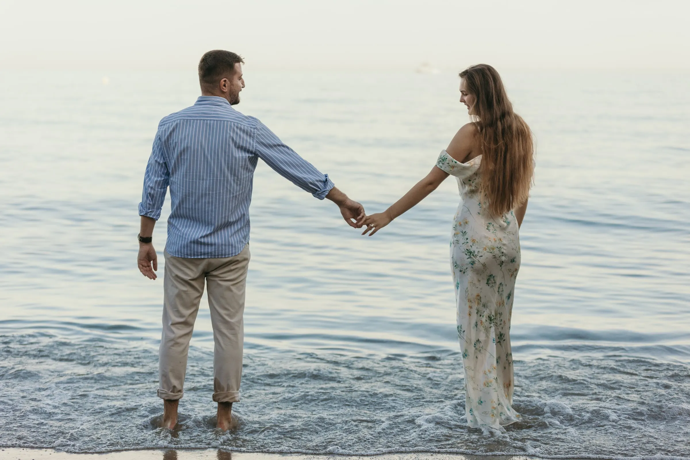 Couple reaching for each other's hands as they wade into the sea, on the beach in Nerja