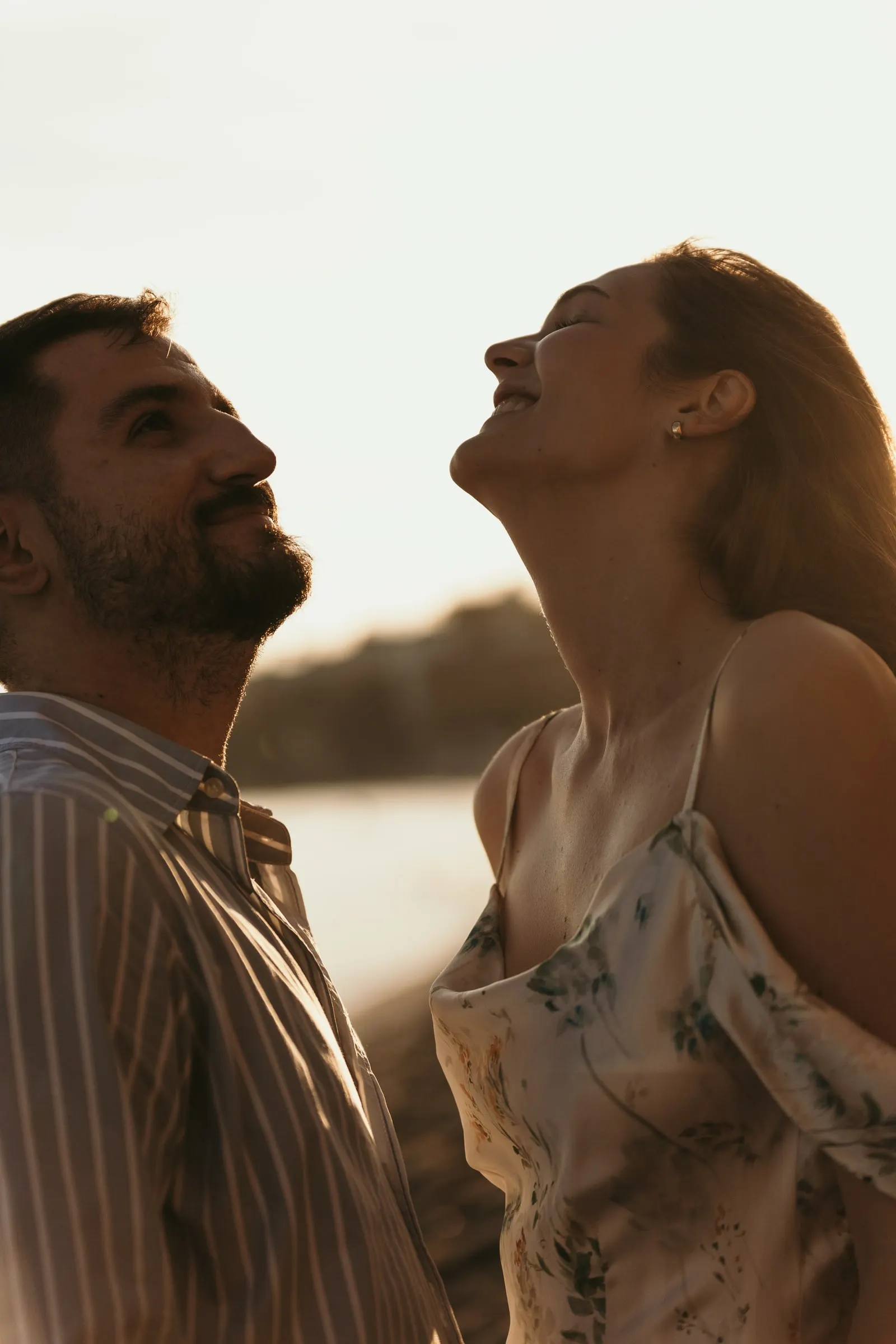 Couple tilting their heads back and laughing in the golden light, on the beach in Nerja