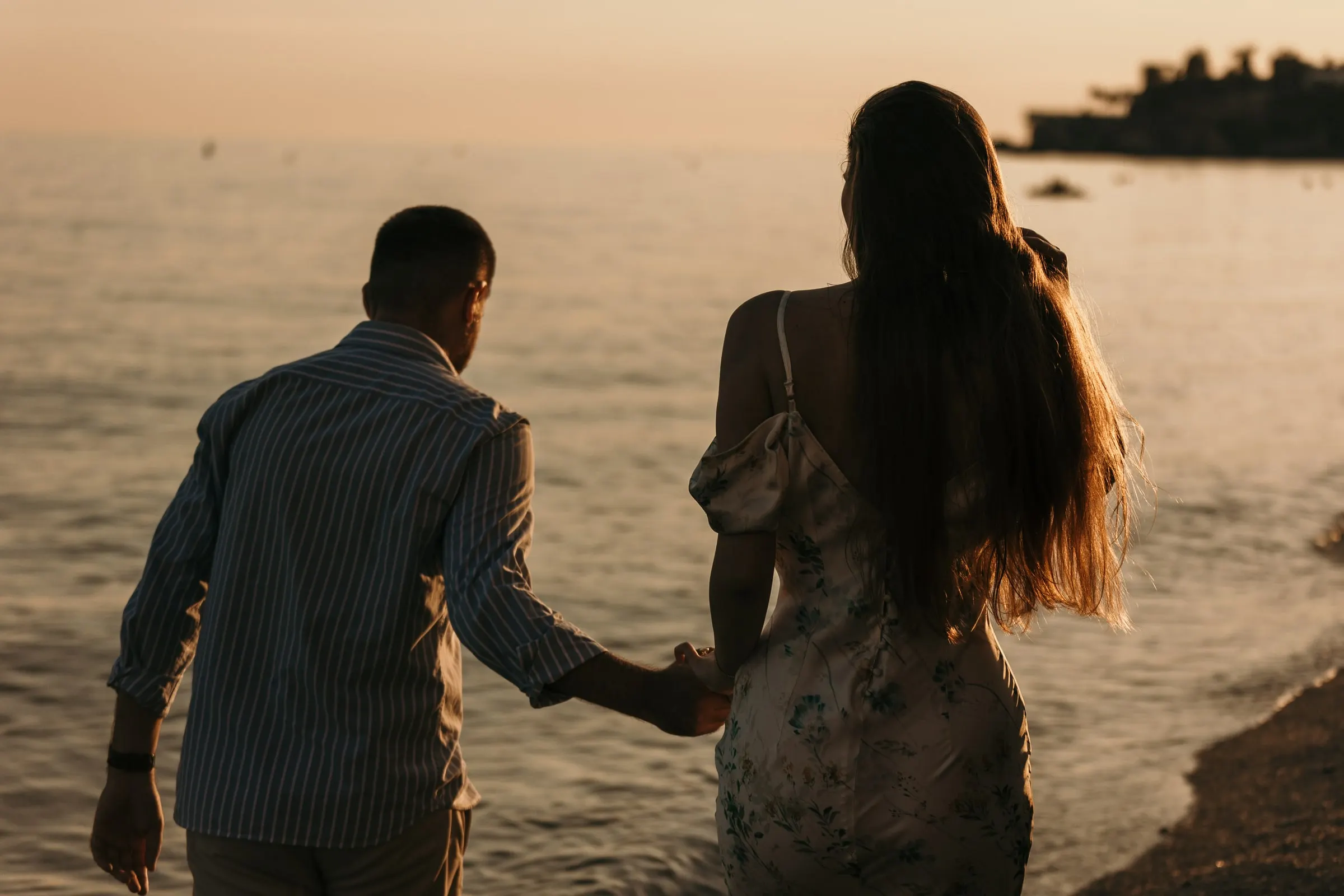 Couple walking hand in hand along the shore at sunset, seen from behind, beach in Nerja