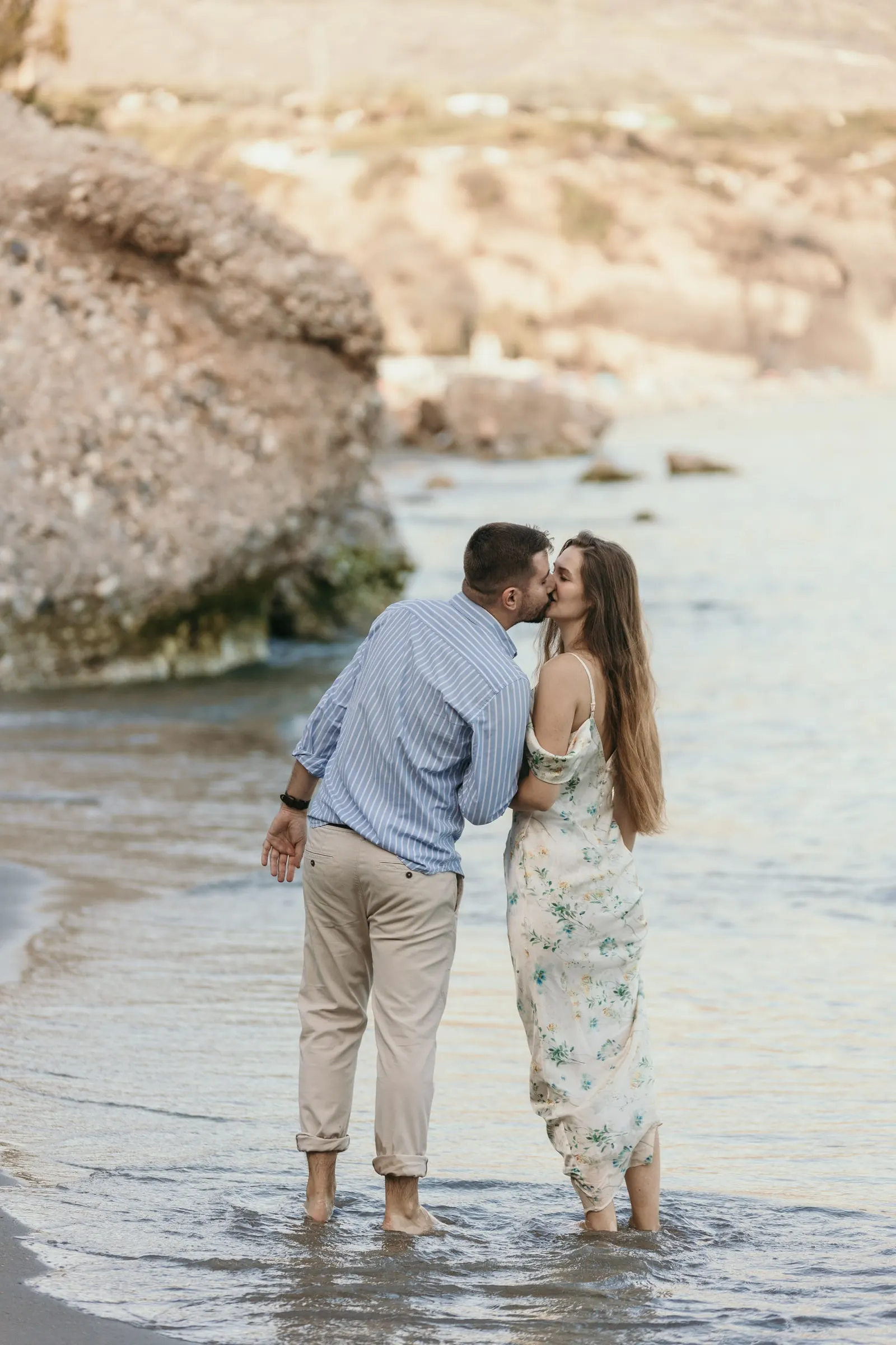 He kisses her as they stand barefoot in the shallows below the rocks, on the beach in Nerja