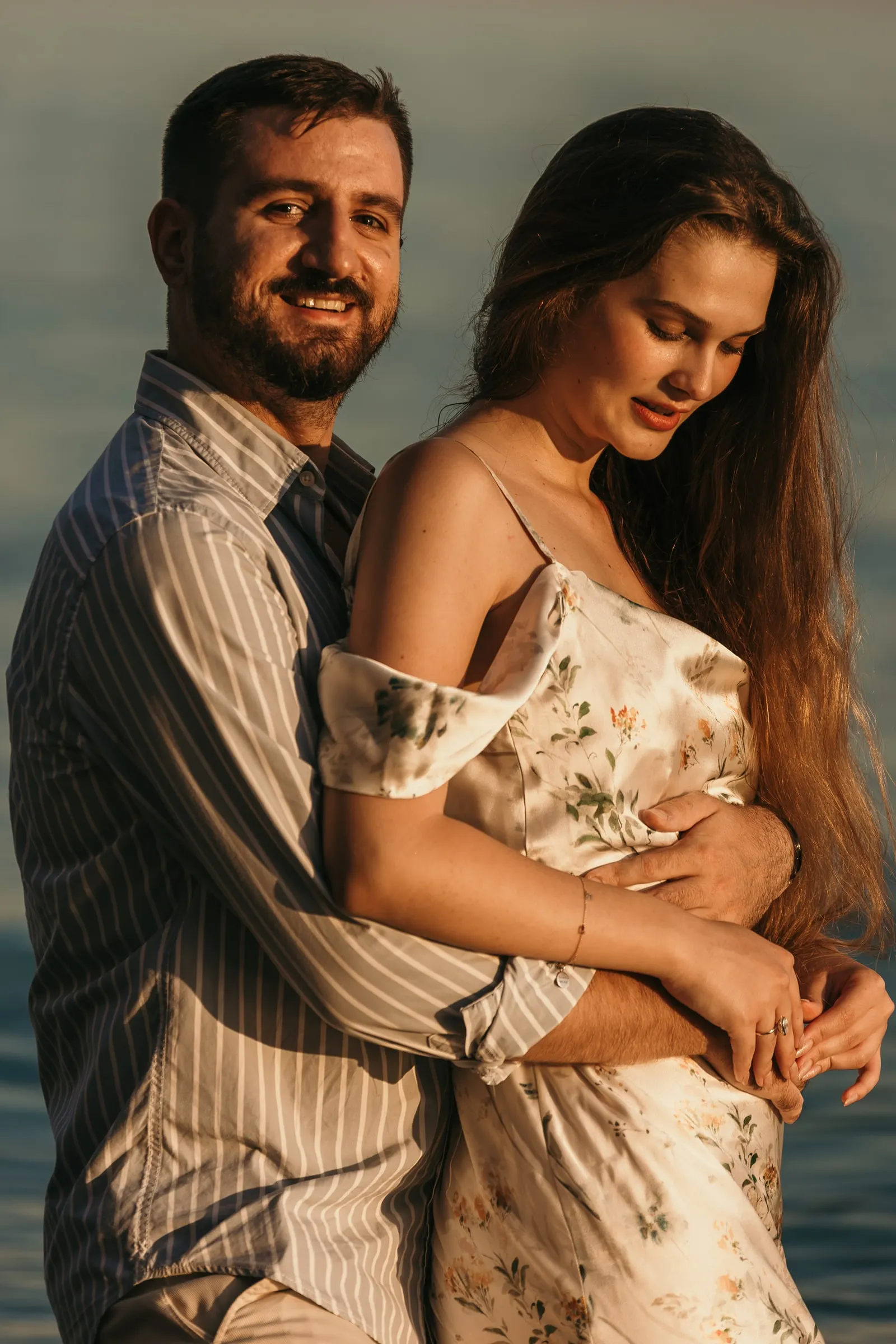 He hugs her from behind, both smiling in the warm evening light, on the beach in Nerja