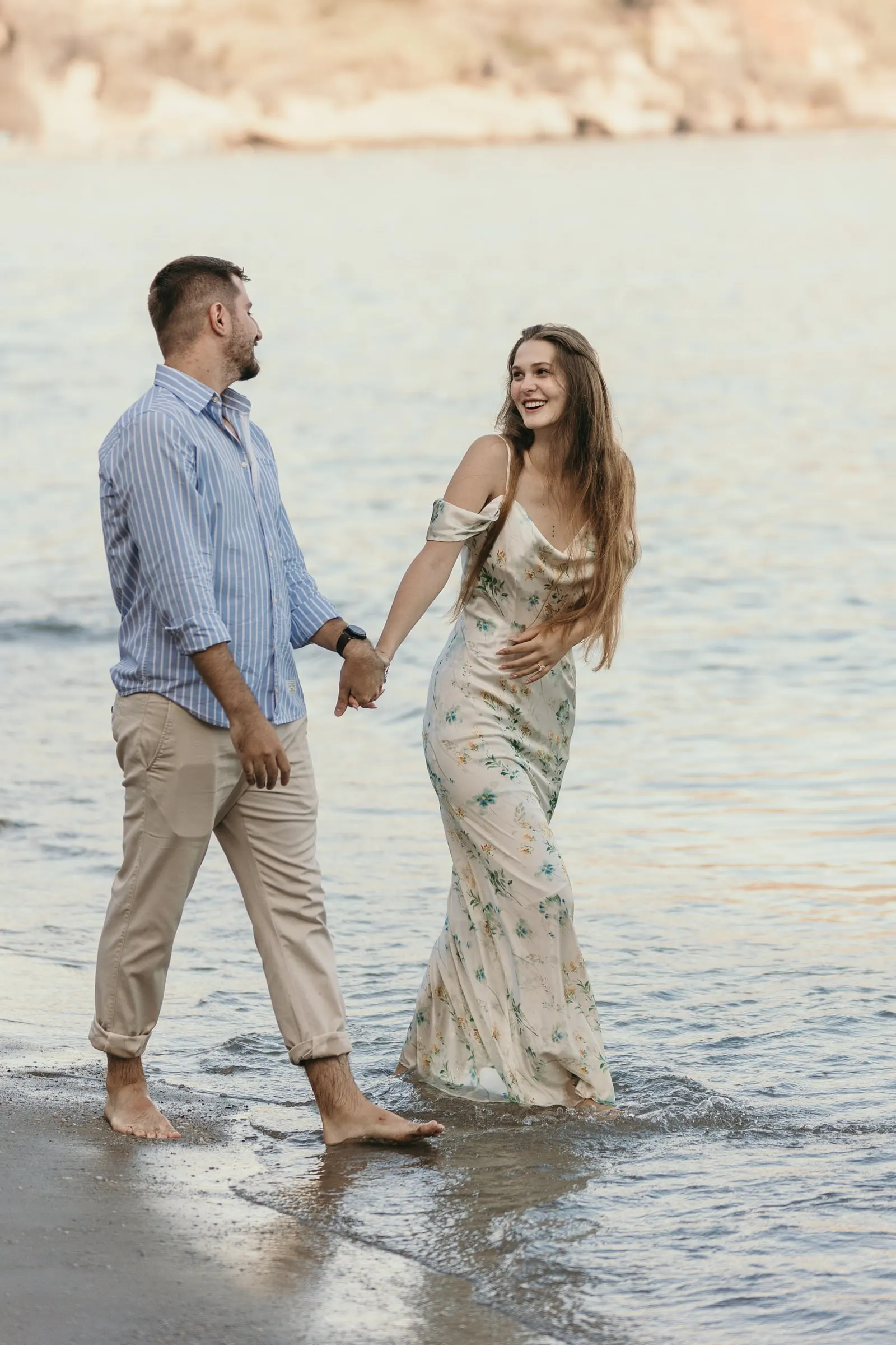 Couple laughing as they walk hand in hand through the shallows, on the beach in Nerja