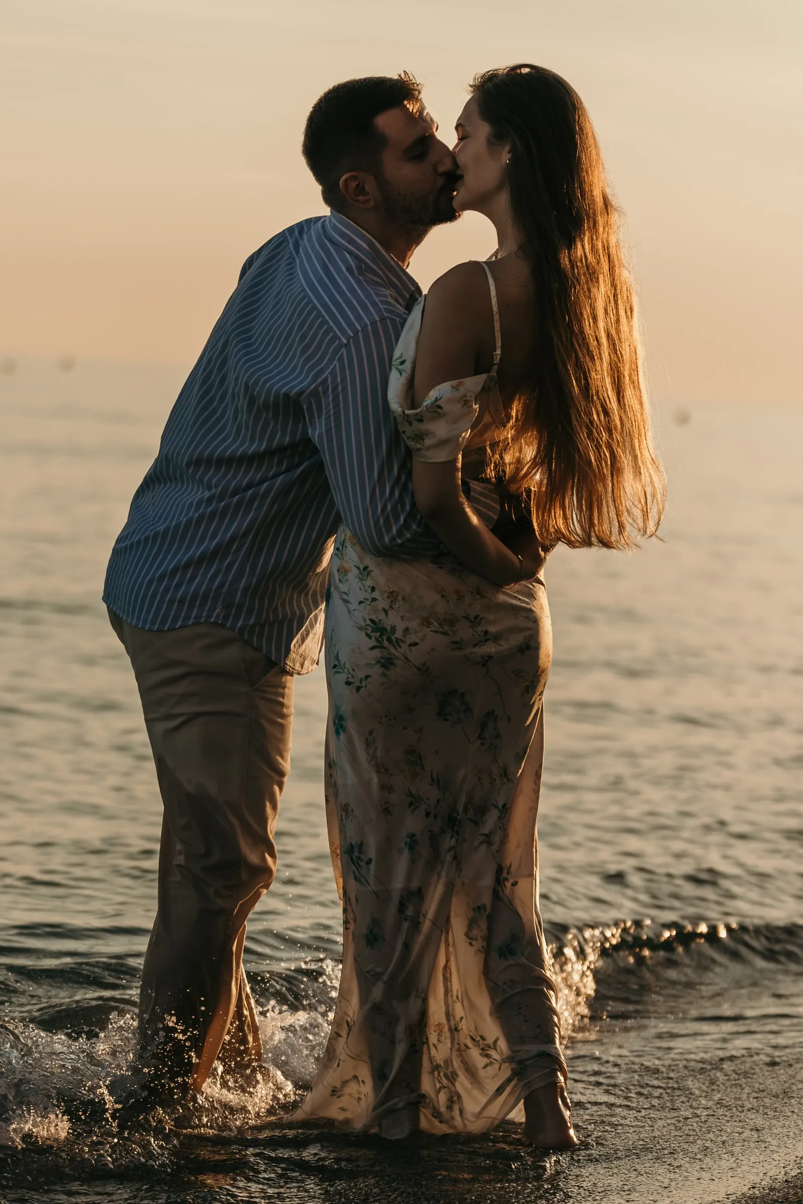Couple kissing as the waves splash around their feet at sunset, on the beach in Nerja