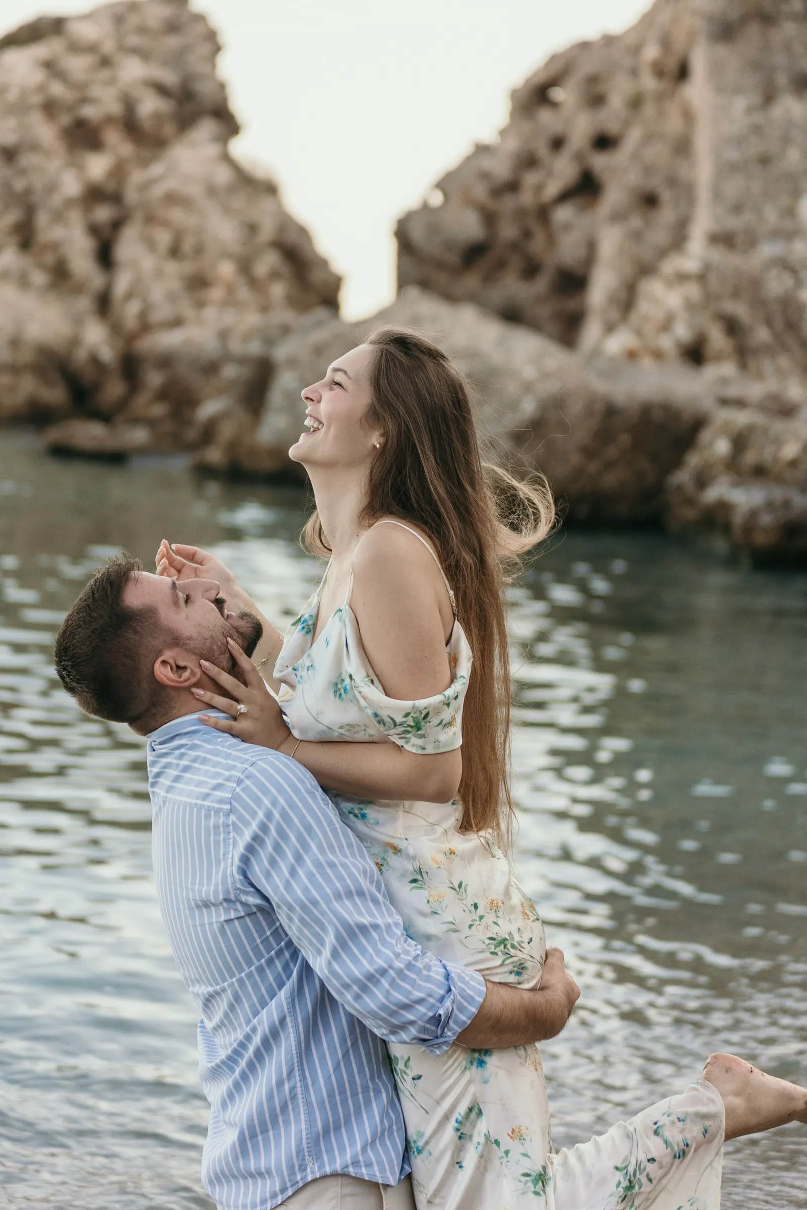 She throws her head back laughing as he lifts her by the rocks, on the beach in Nerja