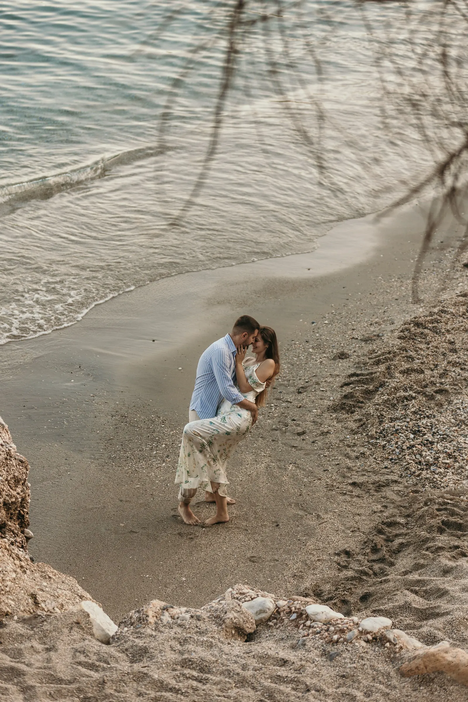High view of the couple embracing on the sand, framed by branches, on the beach in Nerja