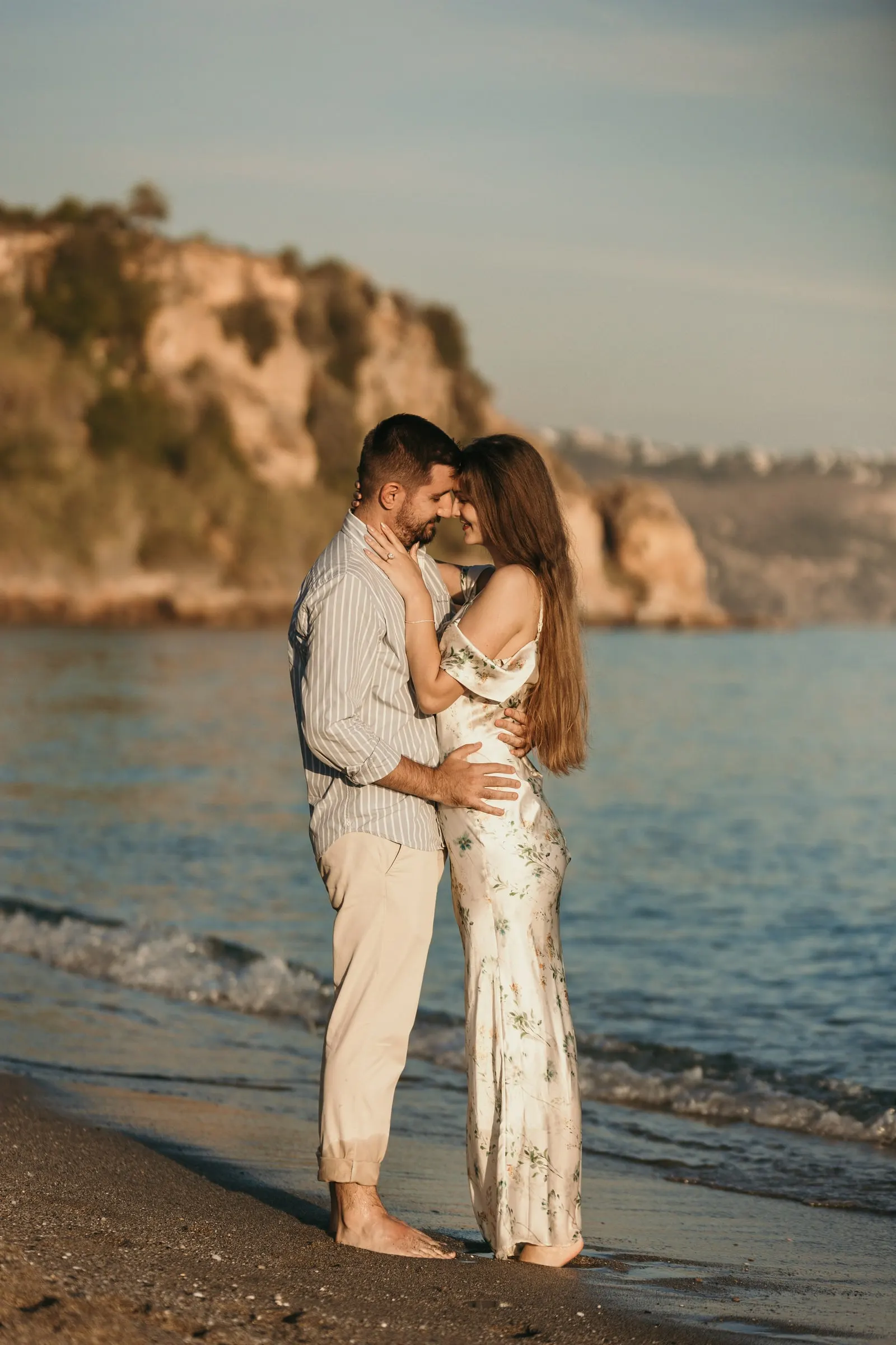 Couple embracing at the water's edge with the cliffs behind, on the beach in Nerja
