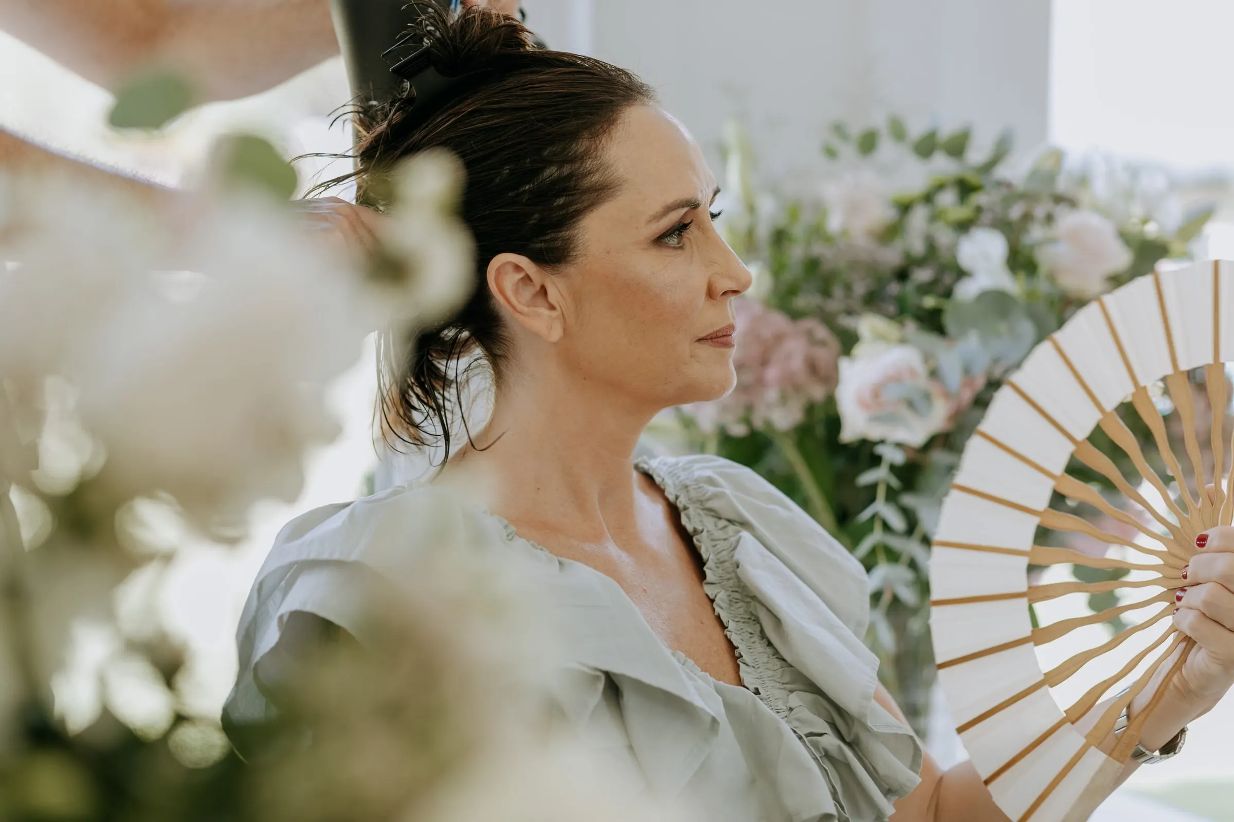 Guest in sage green holding a wooden fan among flowers