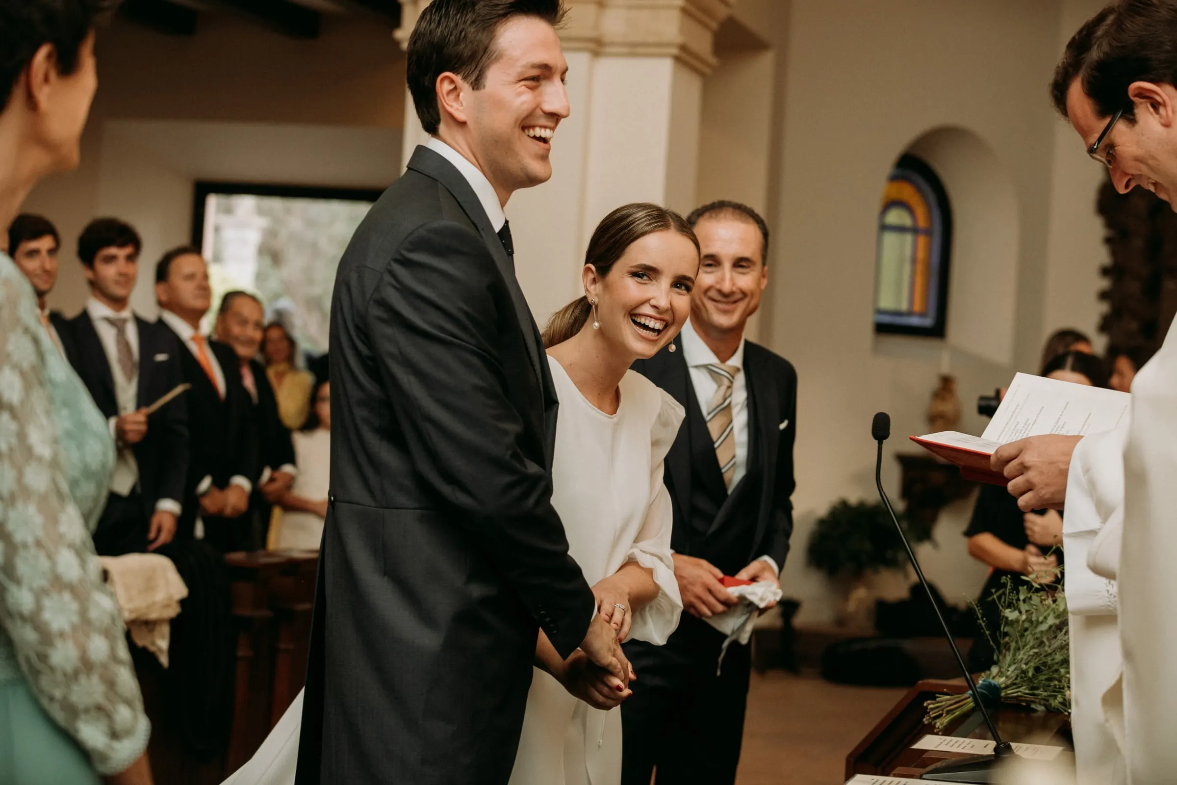 Bride and groom laughing at the altar with guests looking on, Sotogrande