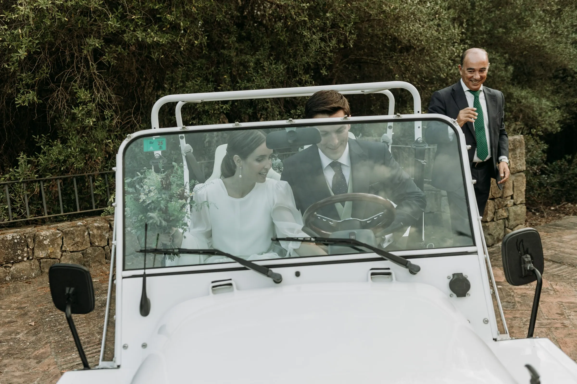 Groom driving the white open-top car with the bride beside him, seen through the windscreen in Sotogrande