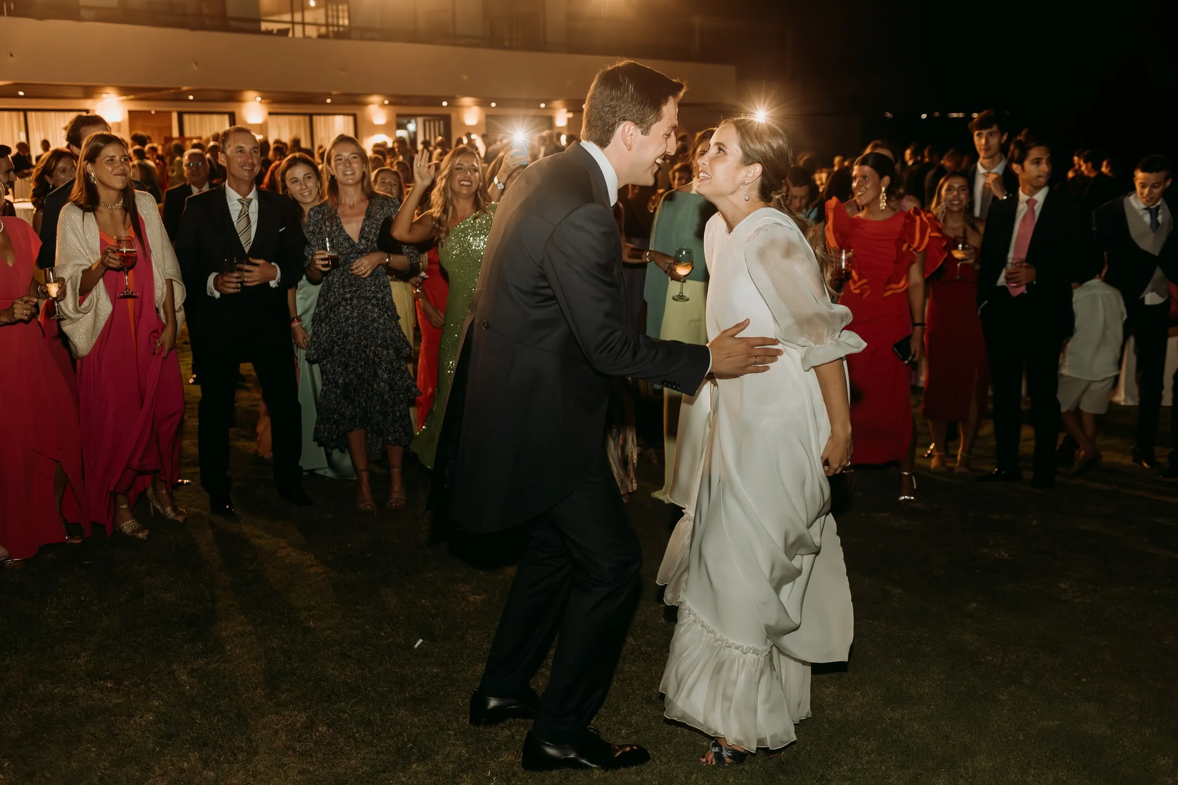Bride and groom starting their first dance on the lawn as guests film with their phones