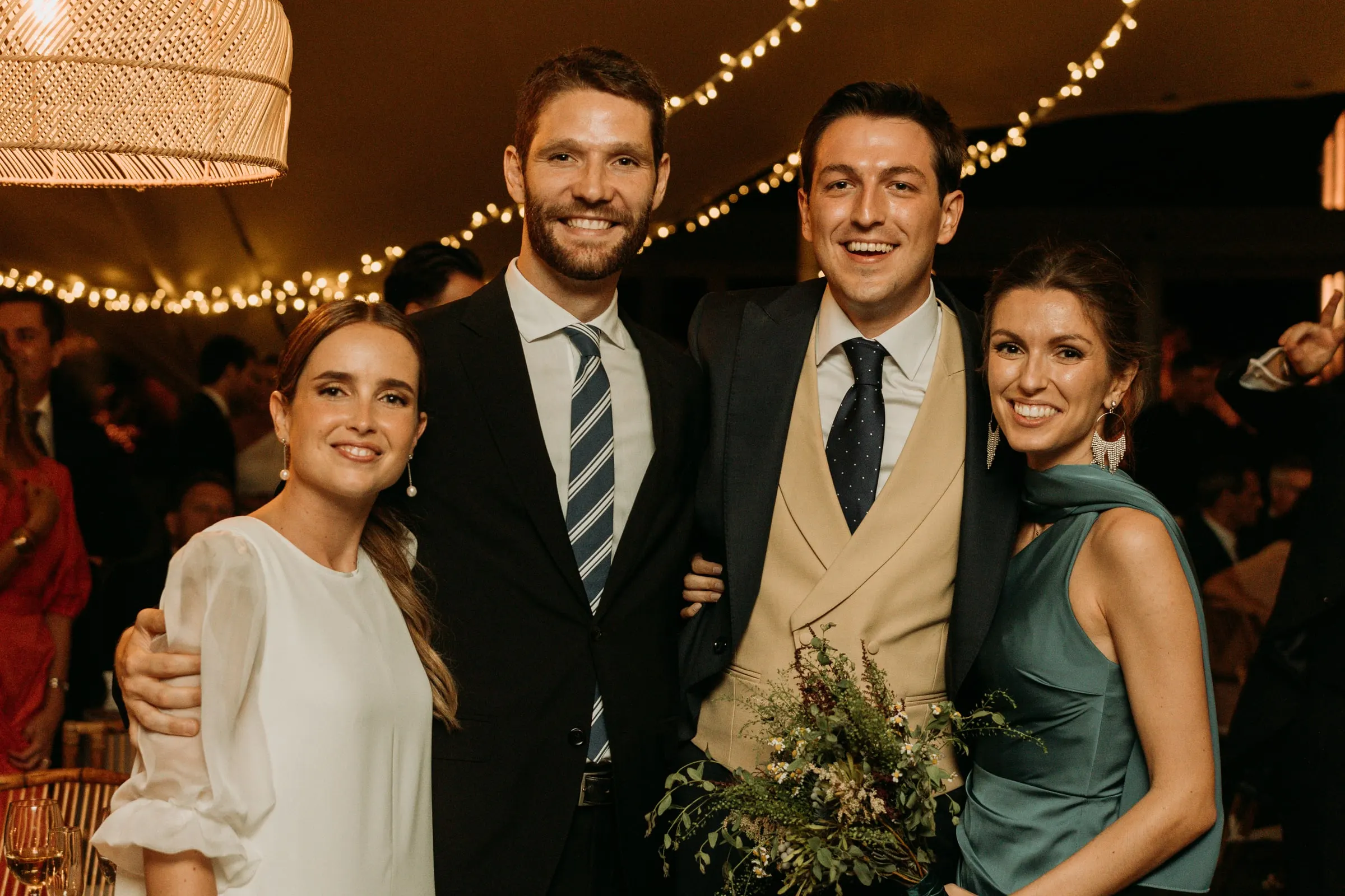 Bride and groom with friends in morning suits and a teal dress under the rattan lamps
