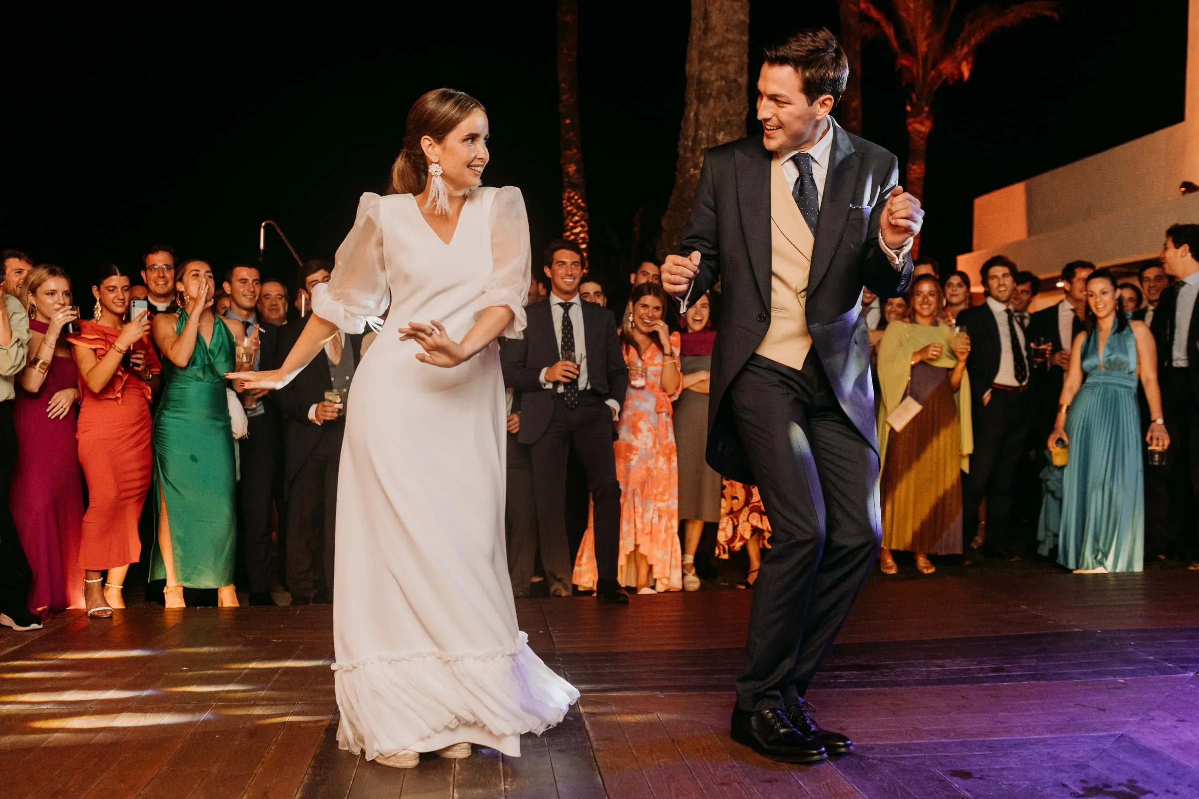 Groom kicking up his heels as he dances with the bride before a crowd of guests in bright dresses, Sotogrande