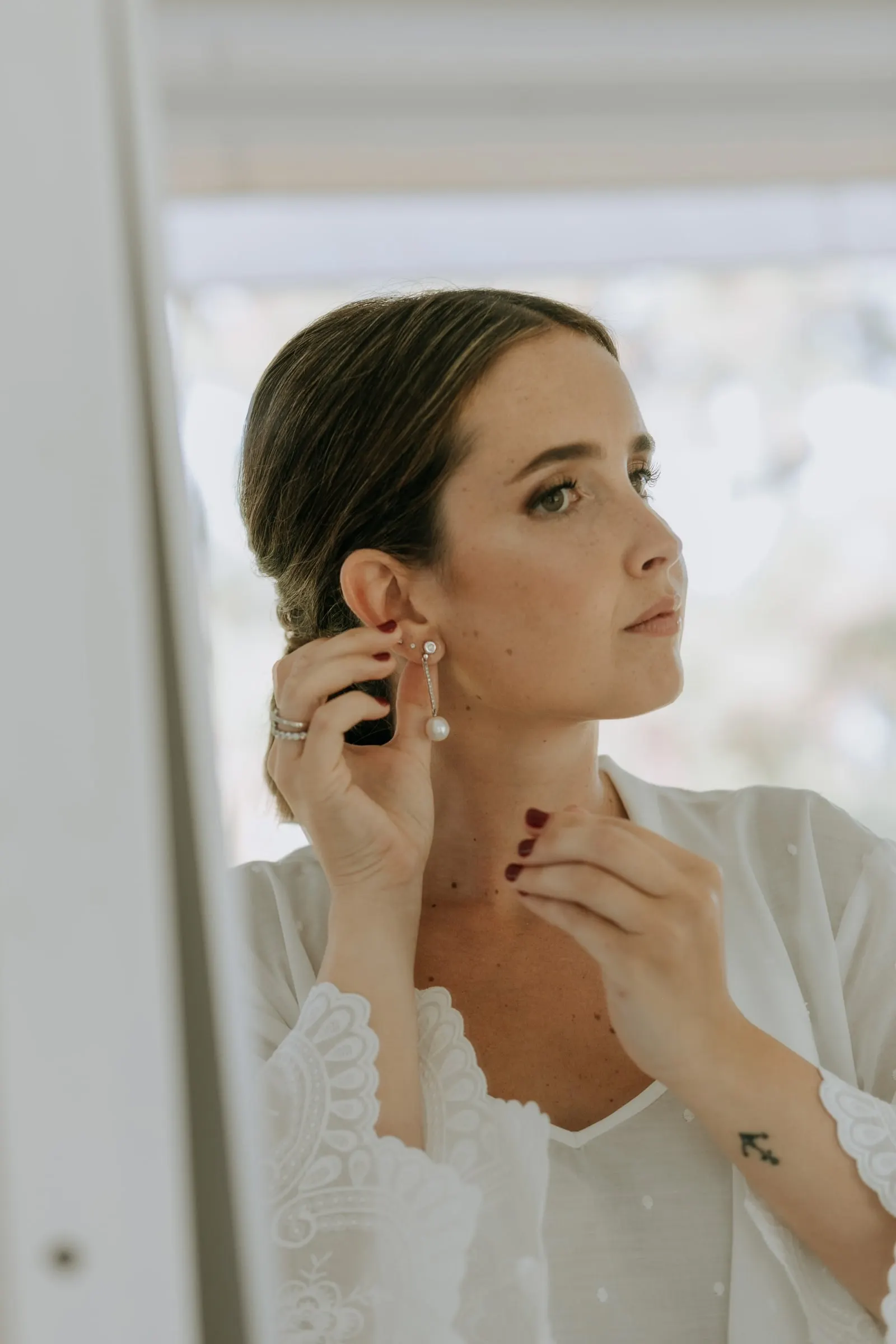 Bride putting on her pearl earrings in her white robe