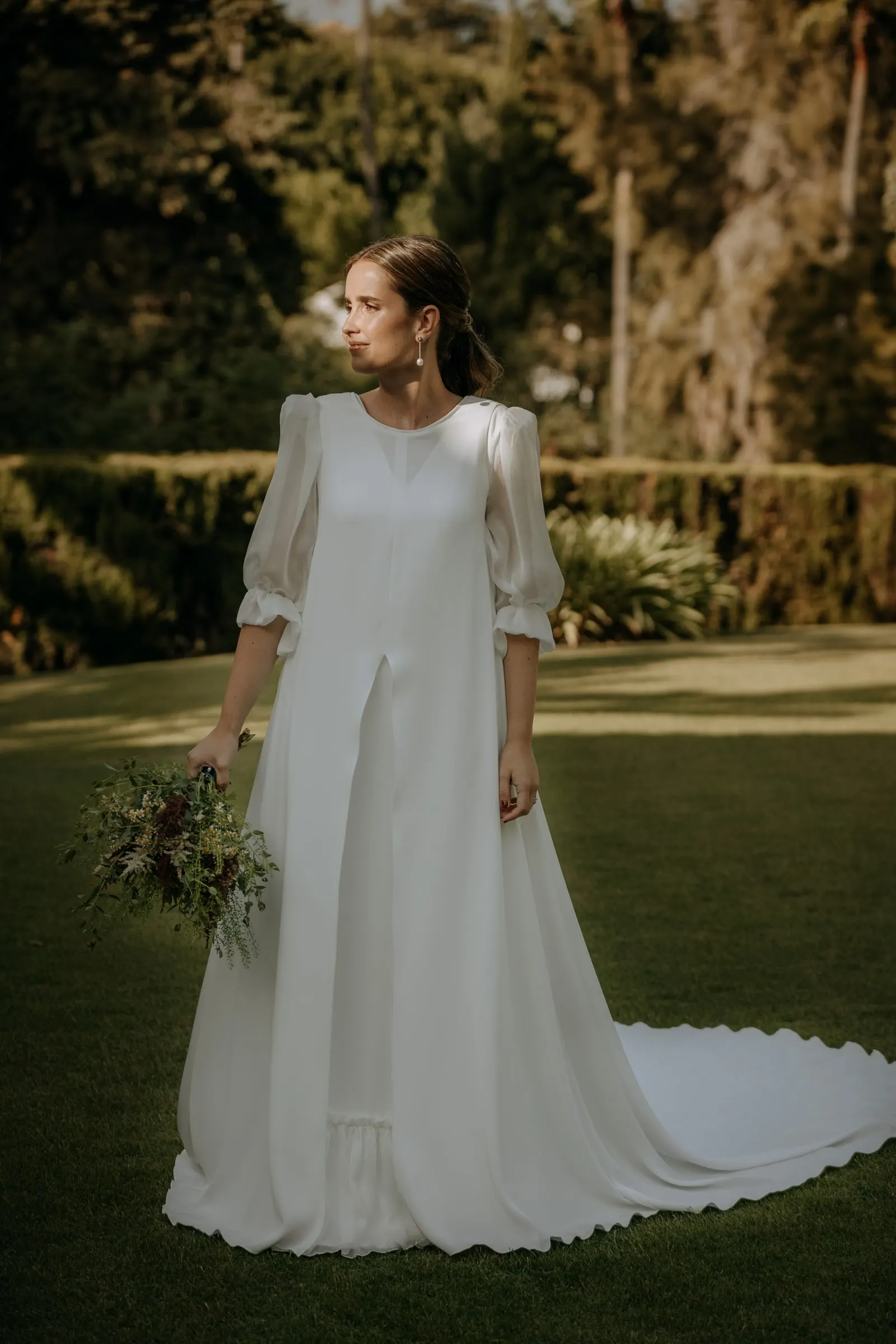 Full-length bride with her long train on the lawn of the family home