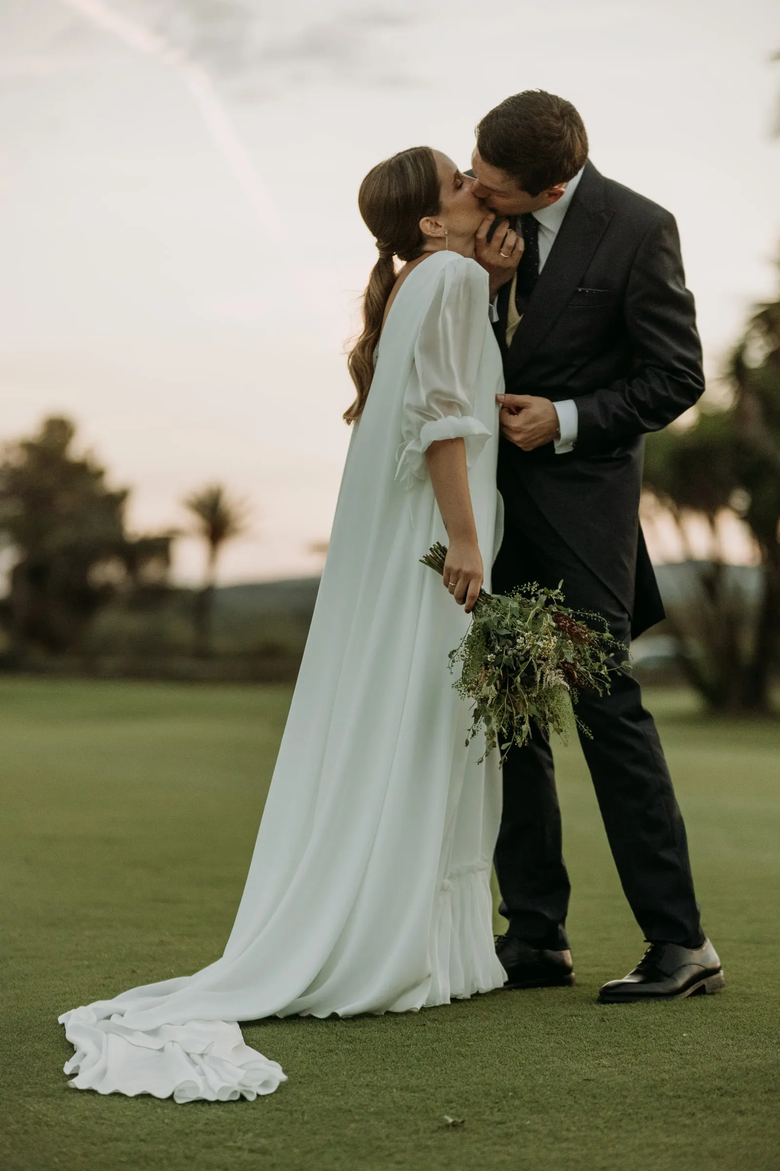 Groom kissing the bride on the golf course, her train across the grass