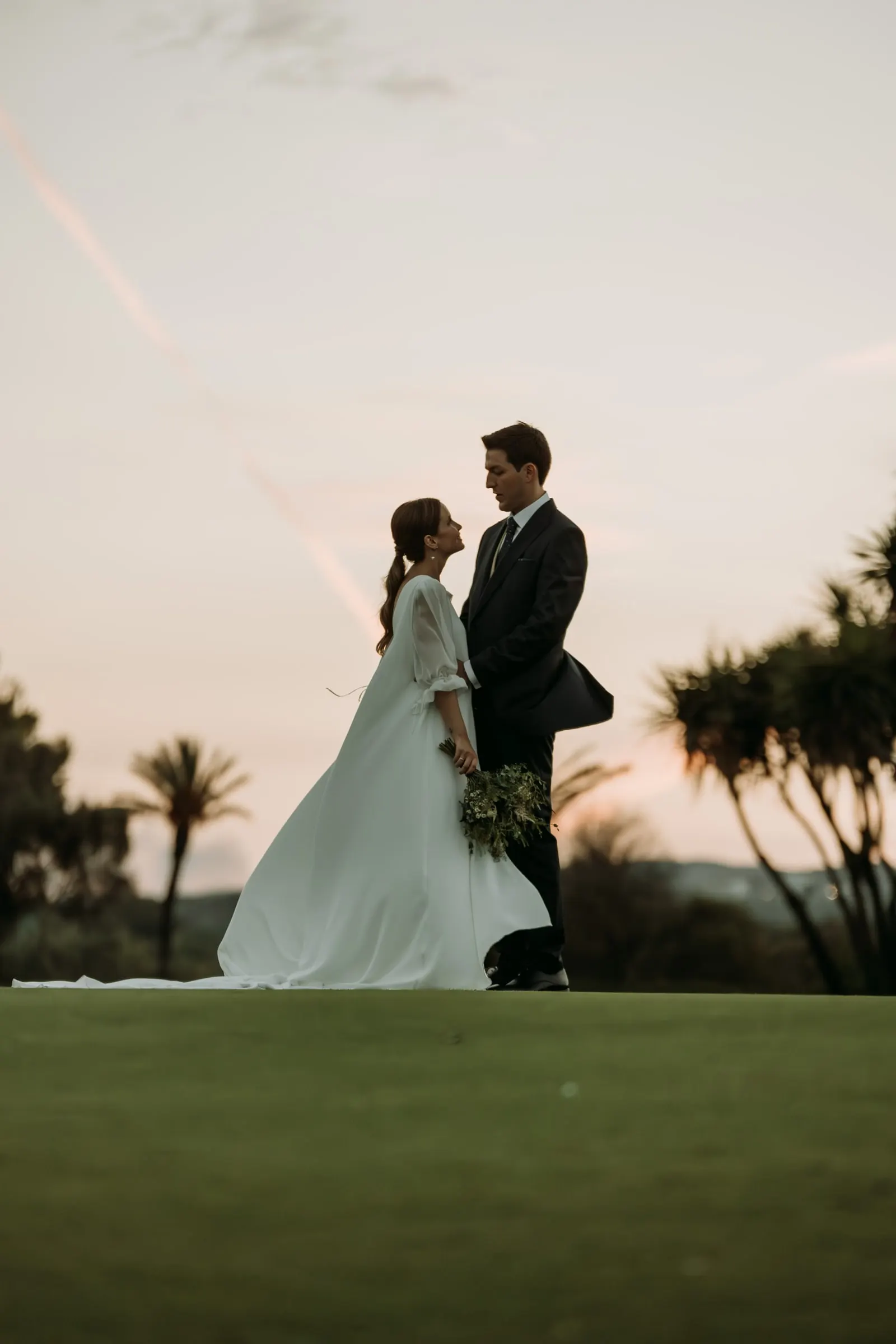 Bride and groom in silhouette against the sunset sky over the palms