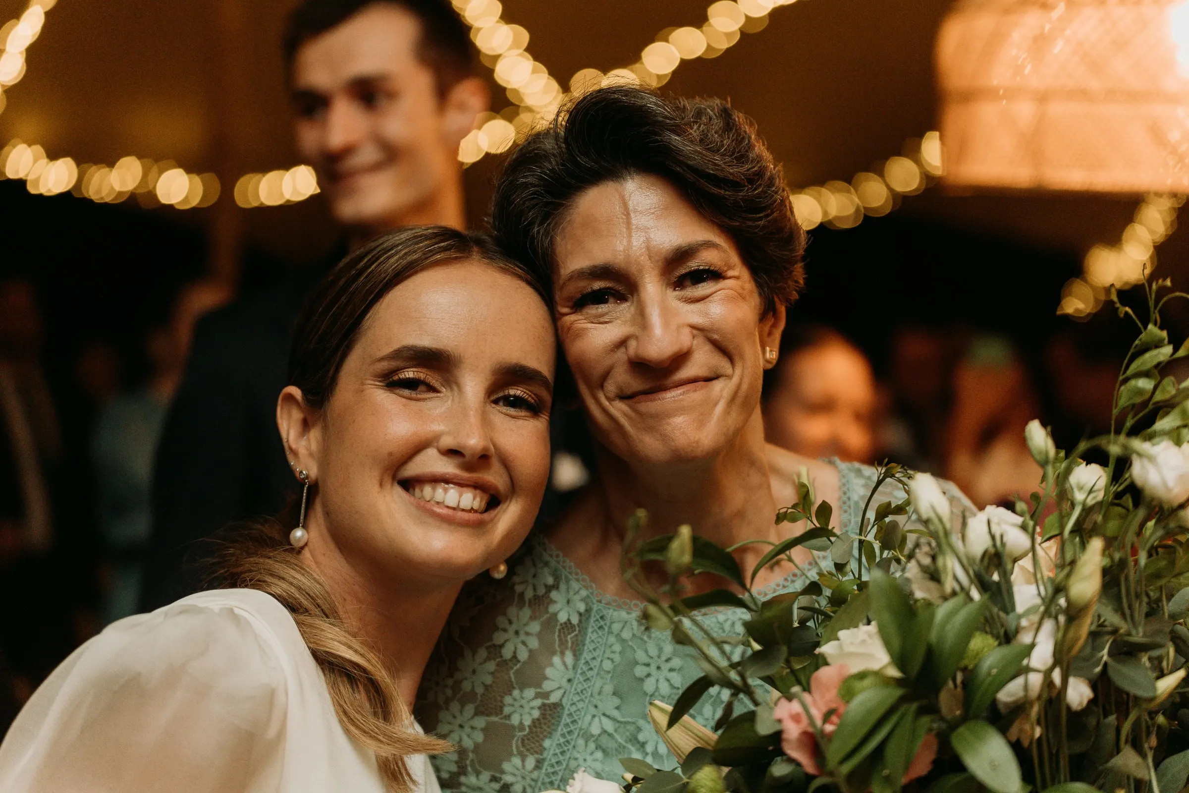 Bride cheek to cheek with a family member, both smiling