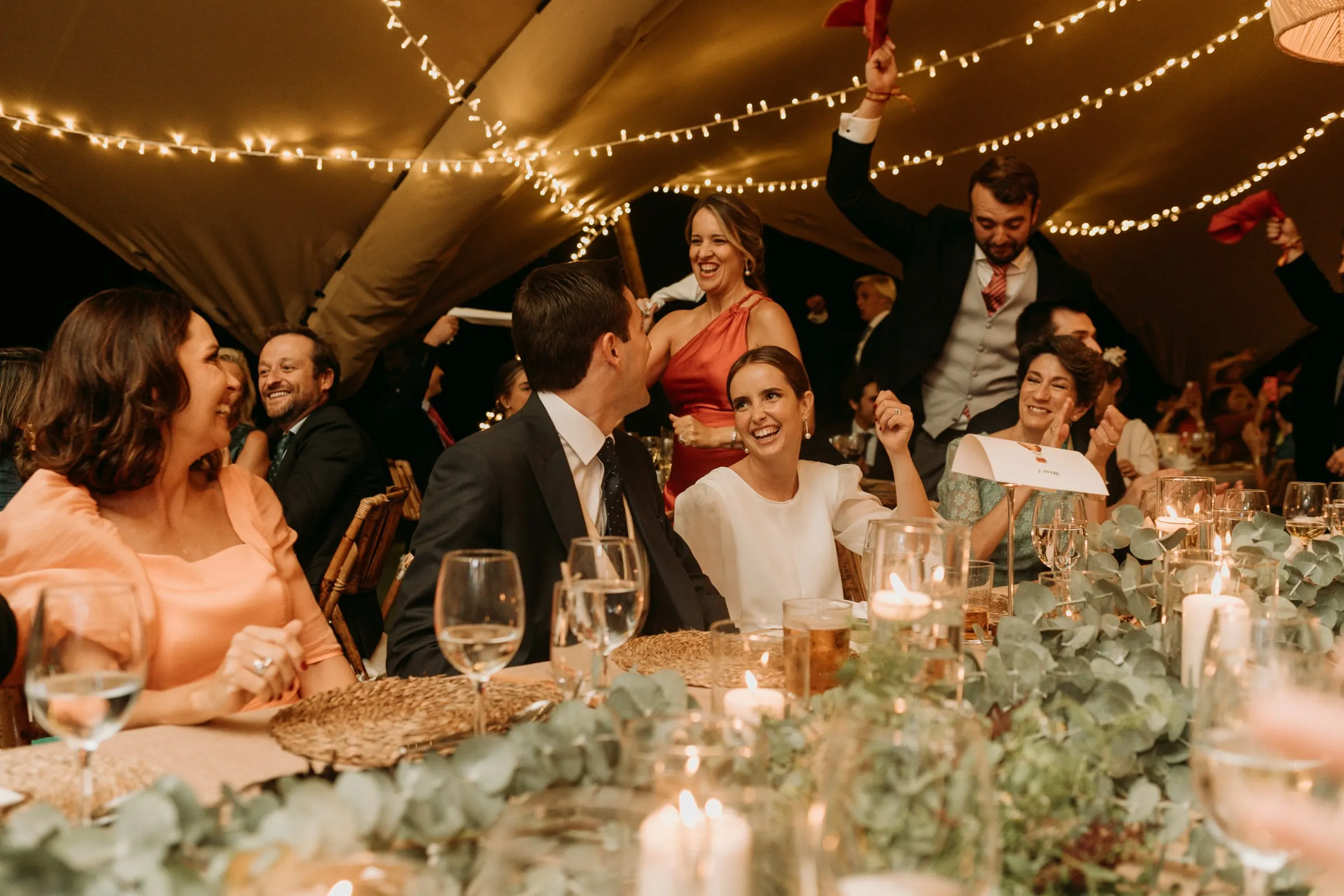 Guests laughing around the candlelit table under the tent