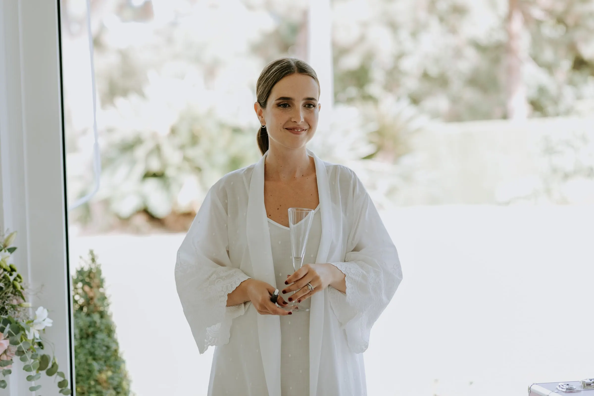 Bride in her white robe standing in the light of the terrace doors on her wedding morning in Sotogrande