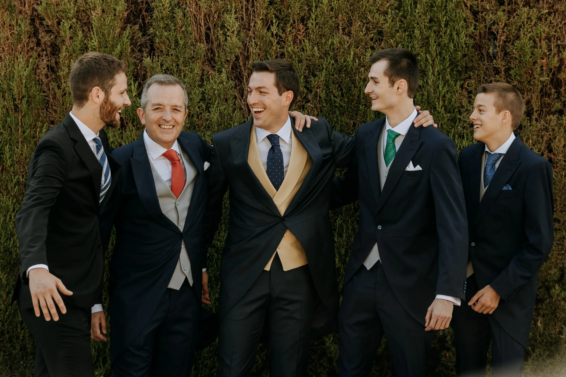 Groom and his groomsmen laughing arm in arm against the garden hedge in Sotogrande