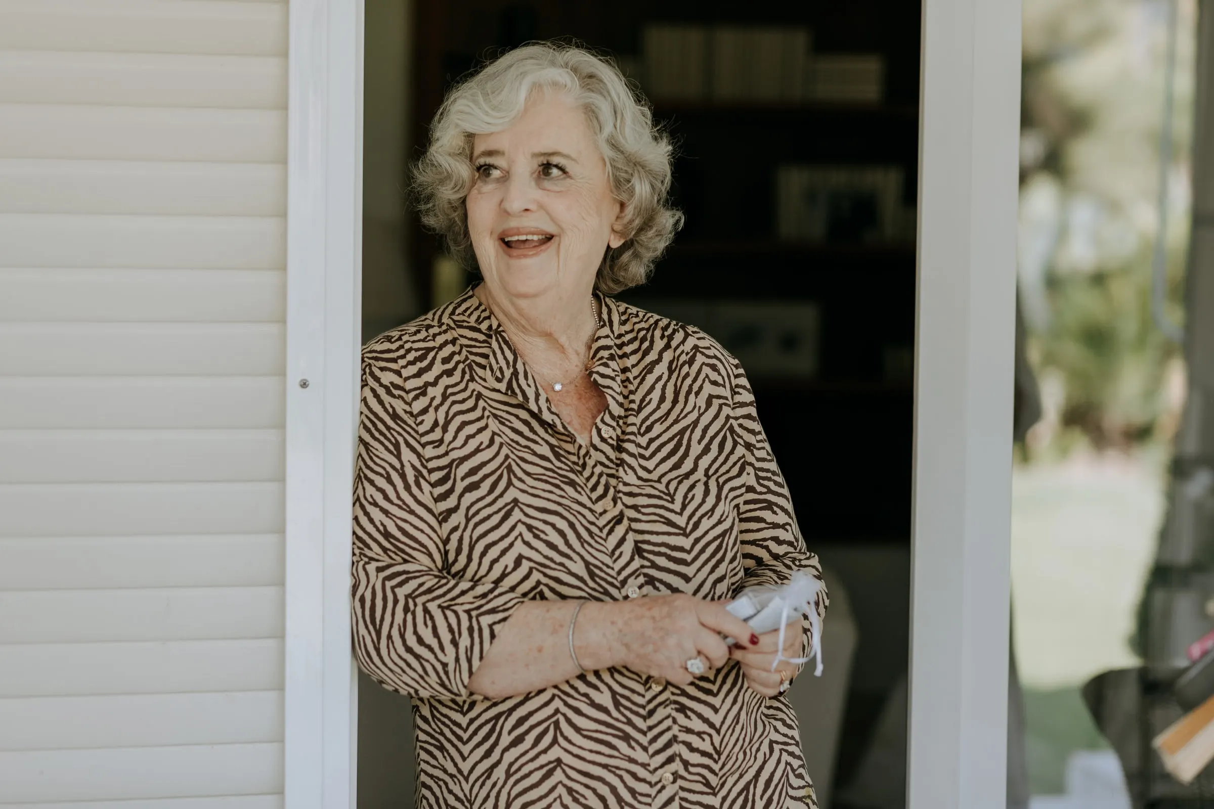 Grandmother in a zebra-print blouse smiling in the doorway of the family home