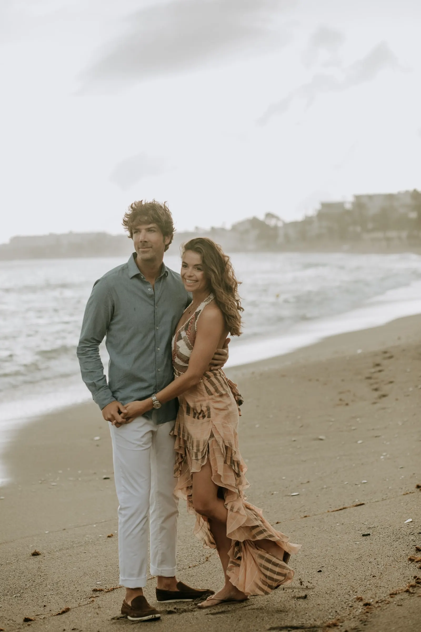 Couple embracing on the sand, she in pink and he in a green shirt, pre-wedding session on the beach, Sotogrande