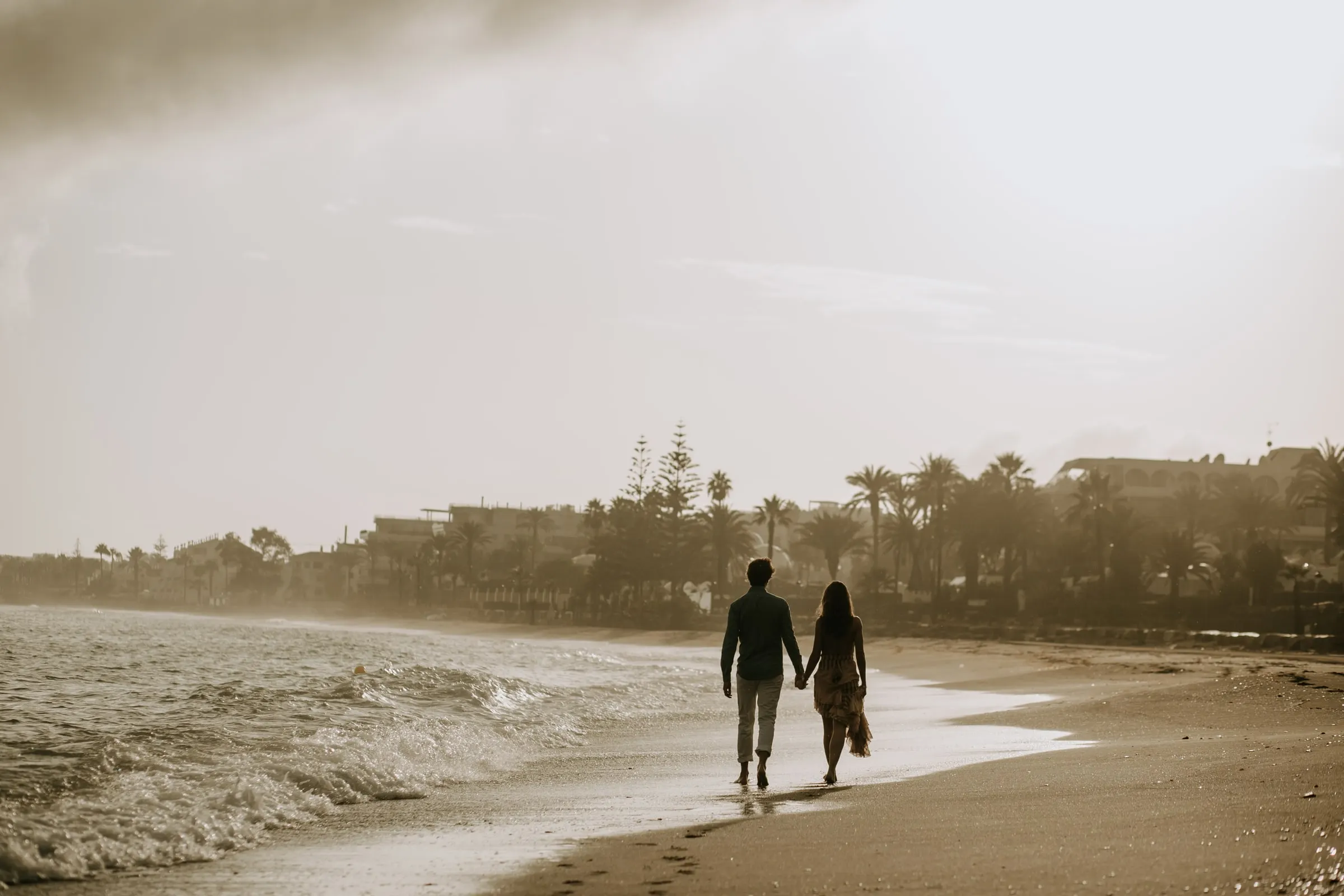 La pareja pasea de la mano por la playa a contraluz, sesión preboda en la playa, Sotogrande