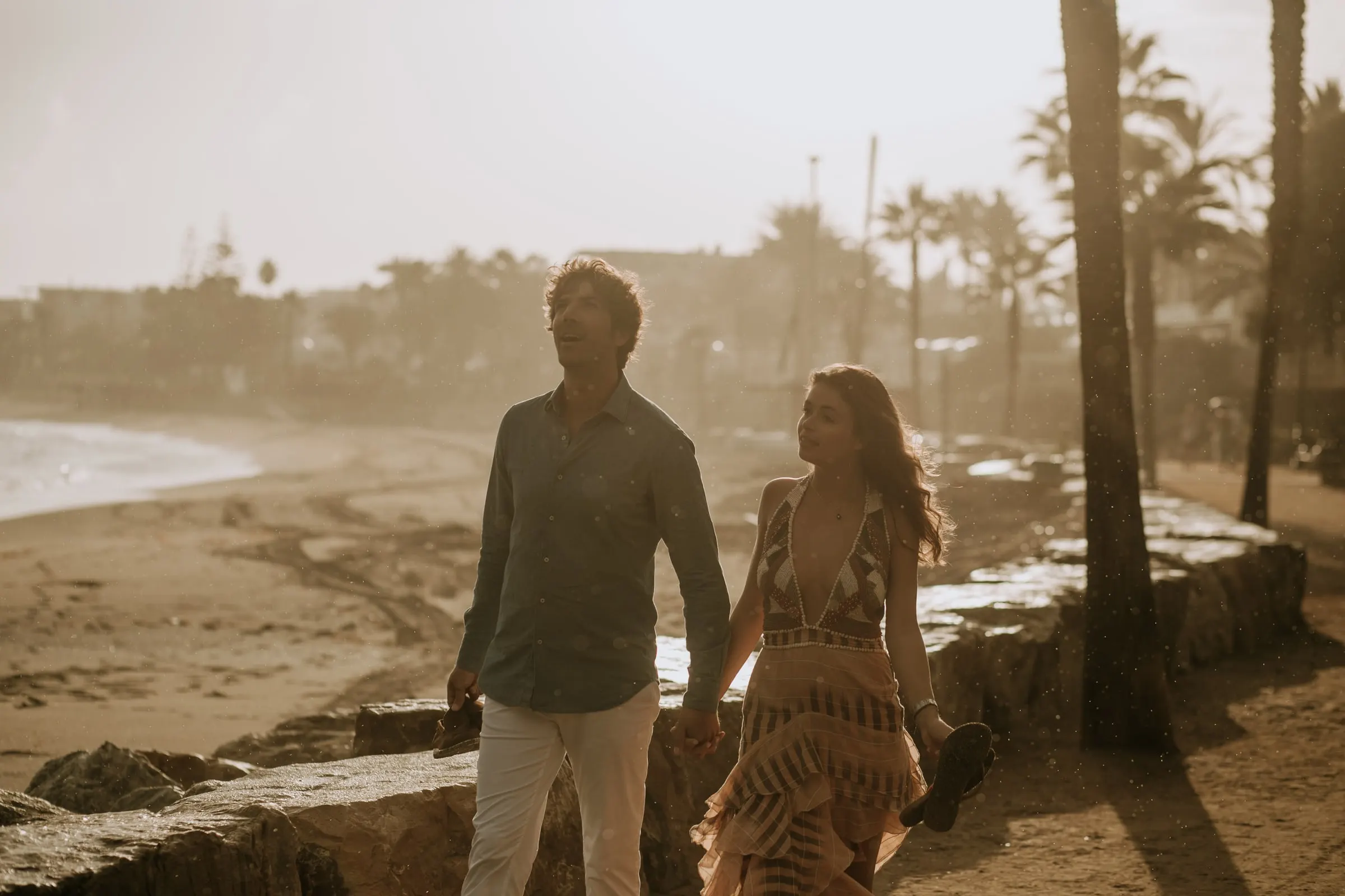 La pareja camina entre palmeras con la luz dorada de la tarde, sesión preboda en la playa, Sotogrande