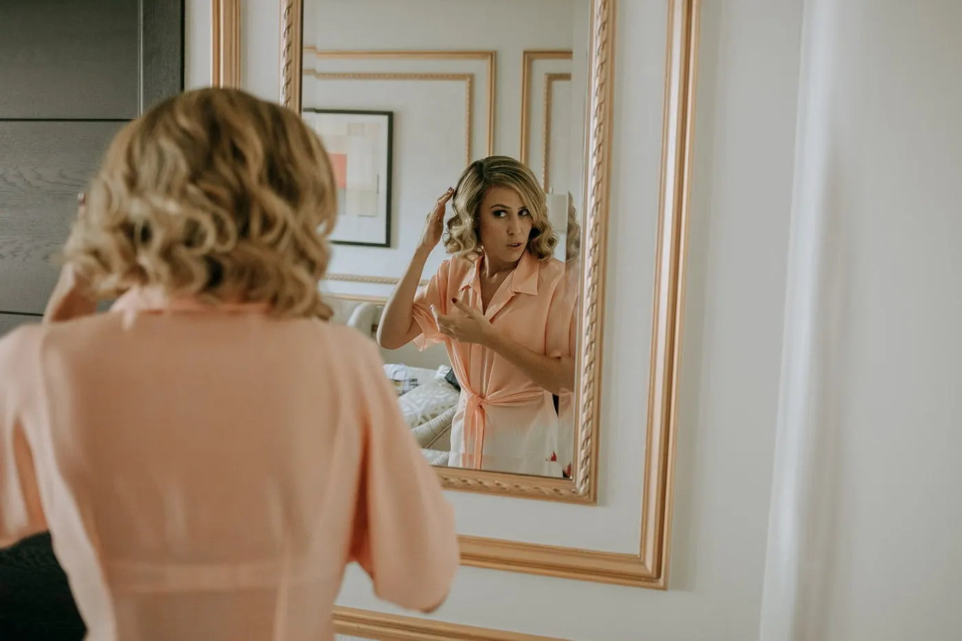 Guest in a peach blouse fixing her hair in a gilded mirror