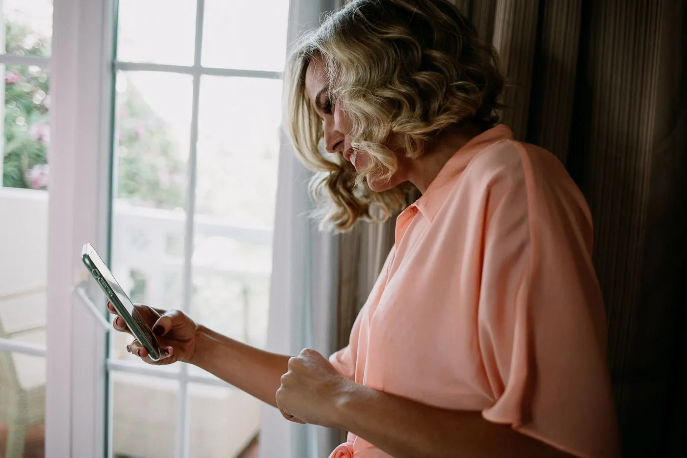 Guest in a peach blouse checking her phone by the window