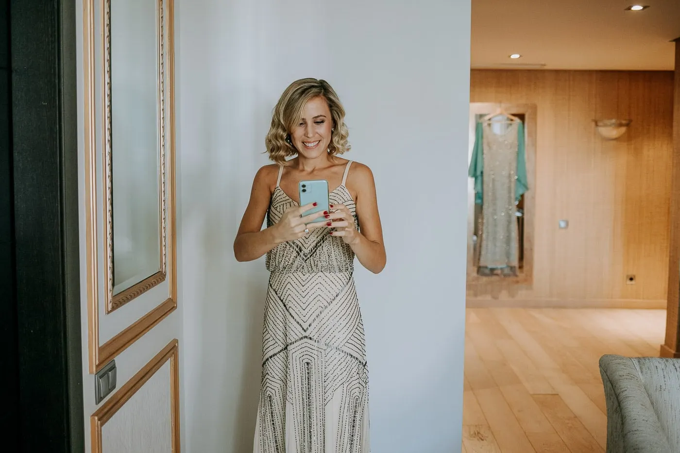 Guest in a beaded dress taking a mirror selfie, the bride's dress behind
