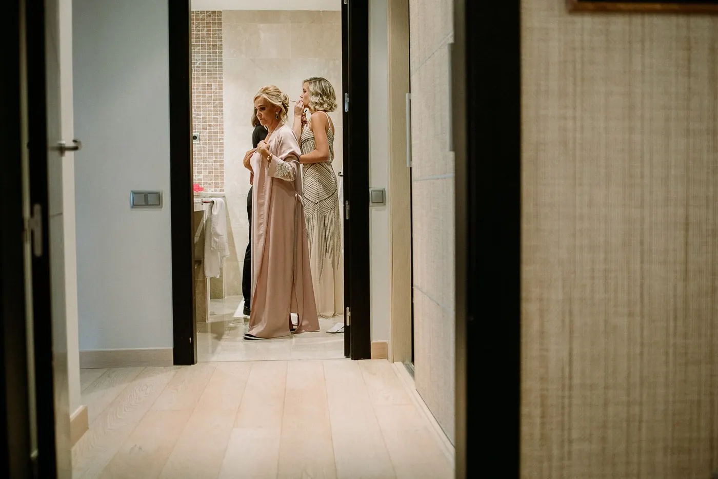 Friends helping the bride into her dress at the end of a corridor