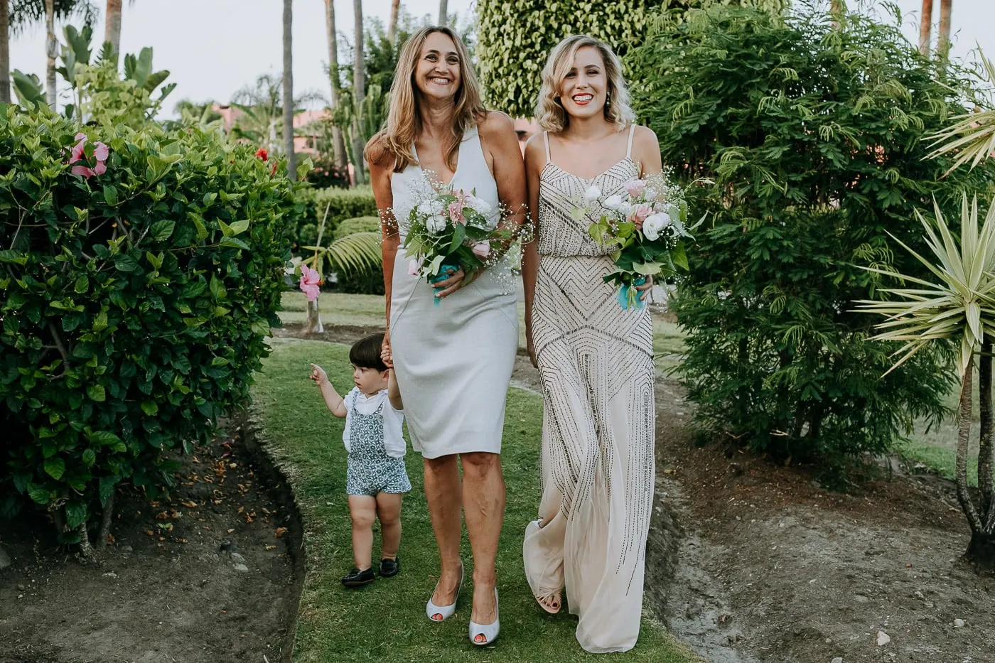 Friends carrying bouquets down the garden path with a toddler
