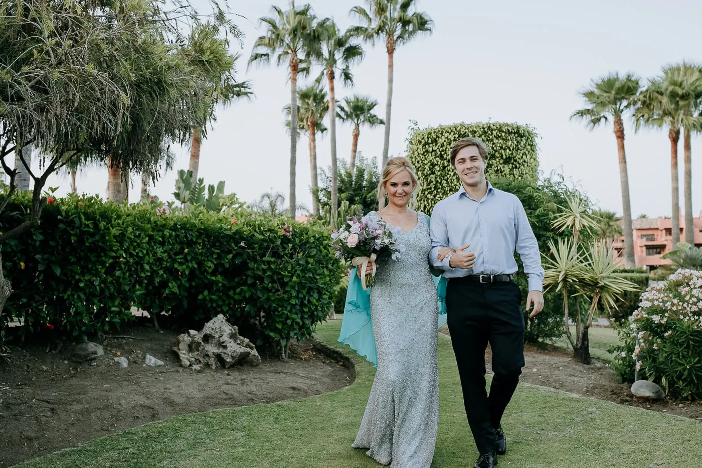 Bride and her escort walking past hedges and palms, Estepona