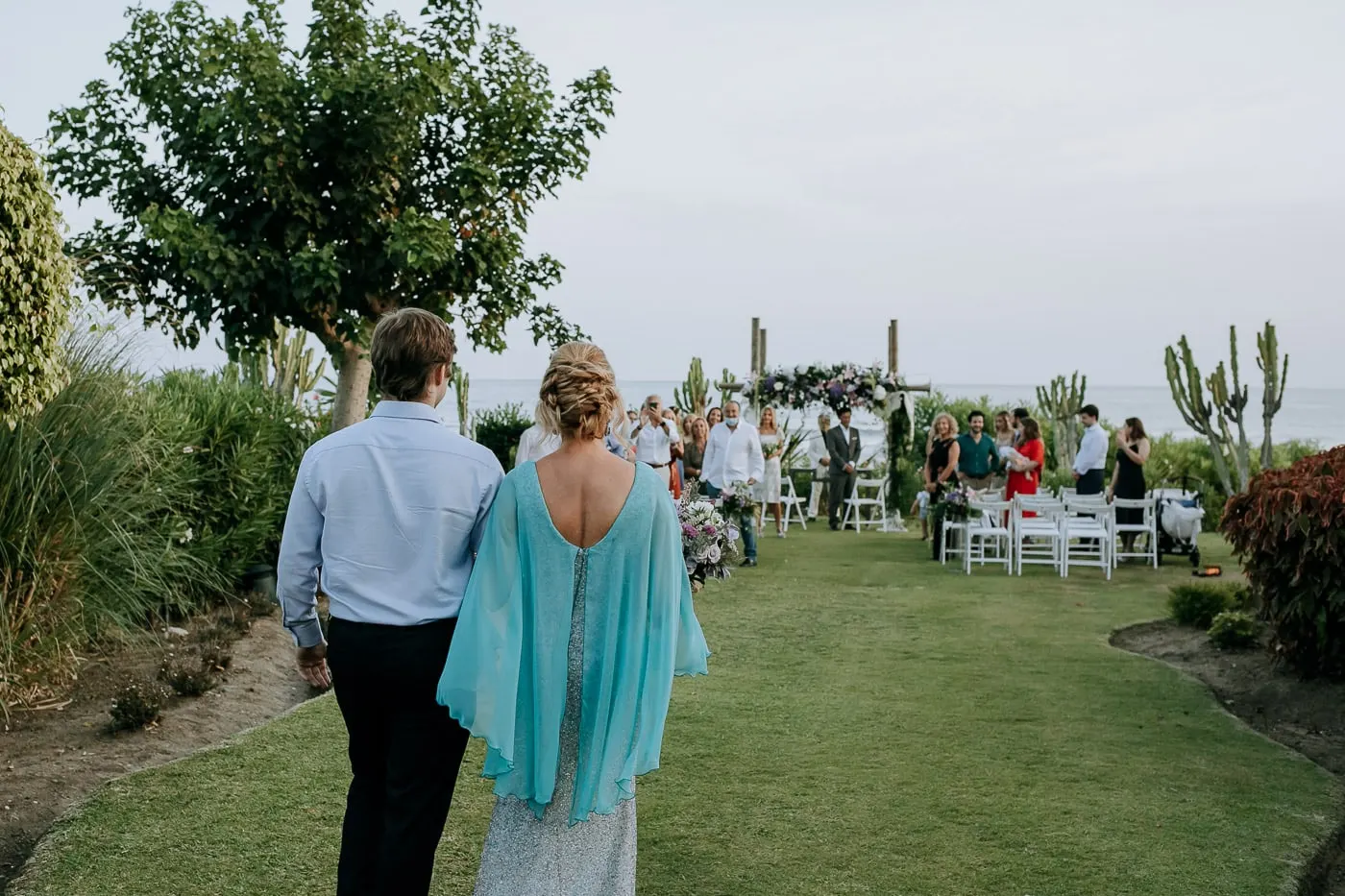 Bride seen from behind walking towards the guests and the flower arch