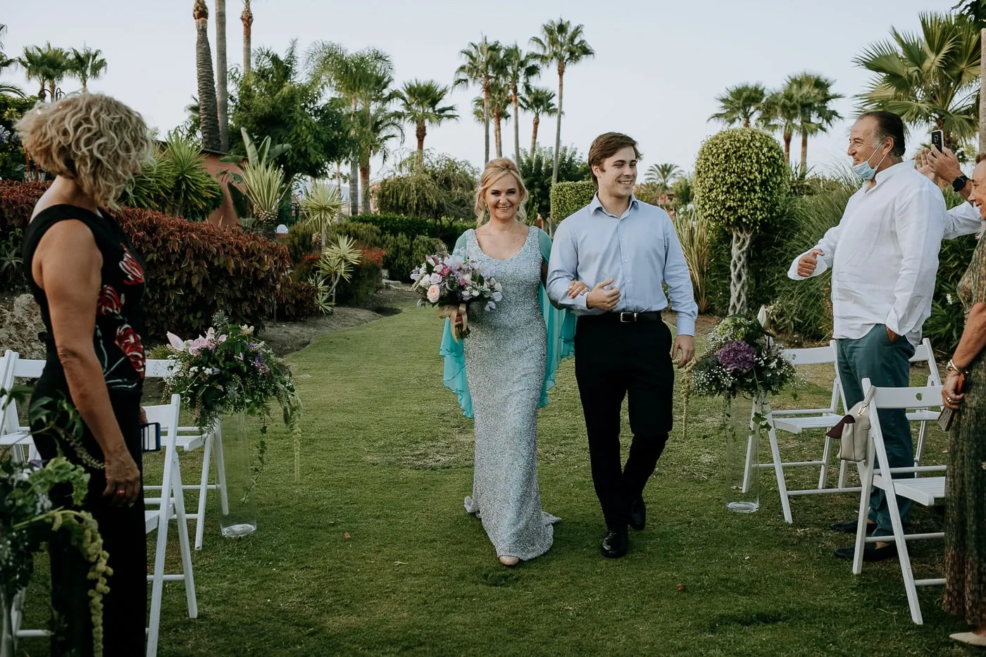 Bride walking down the aisle between bouquets tied to the chairs