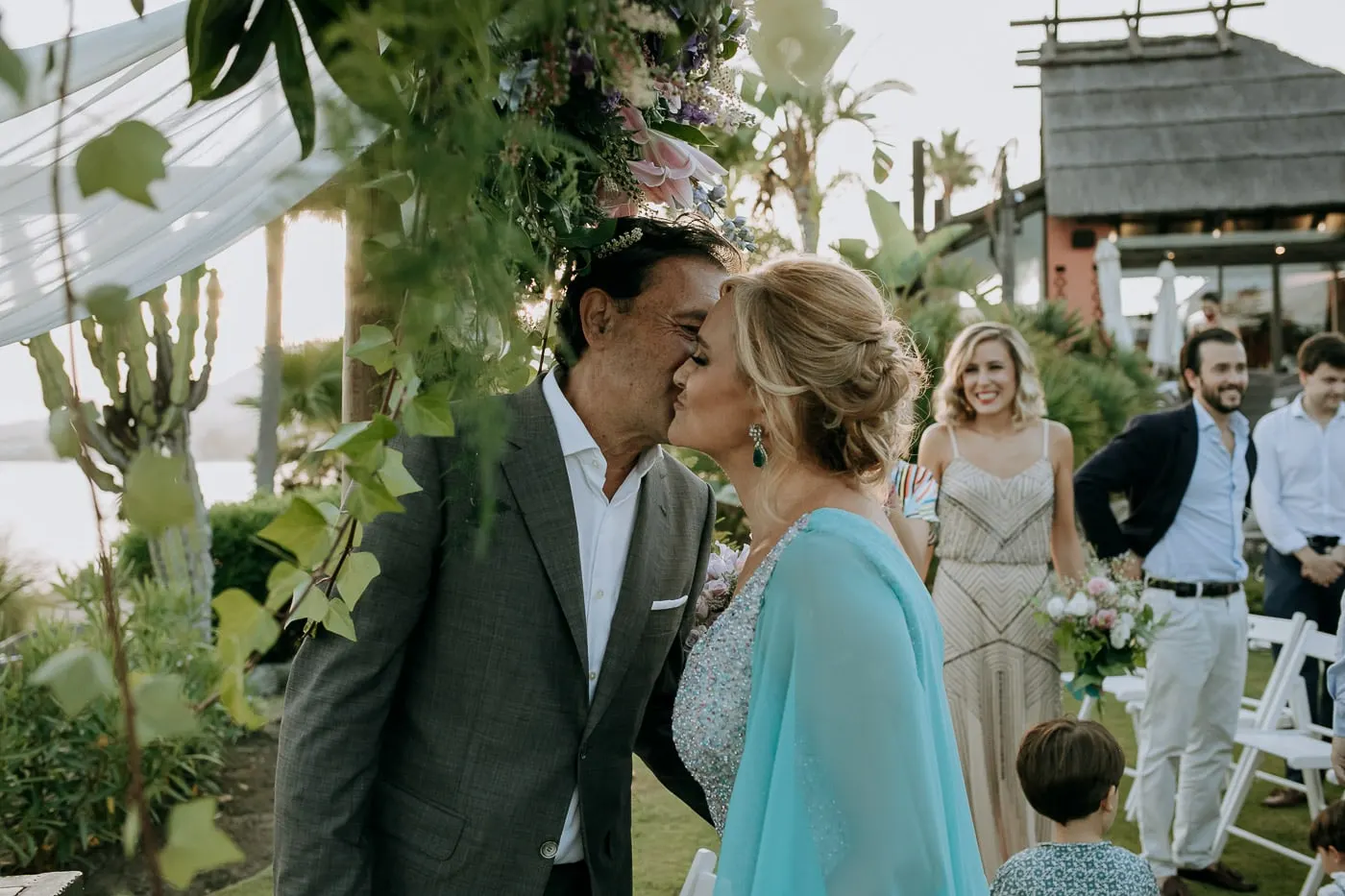 Groom greeting the bride with a kiss on the cheek by the arch