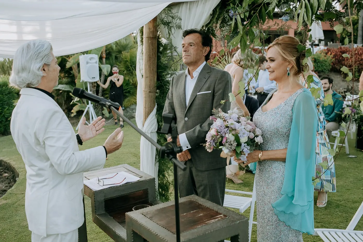Officiant in a white suit speaking to the couple at the microphone