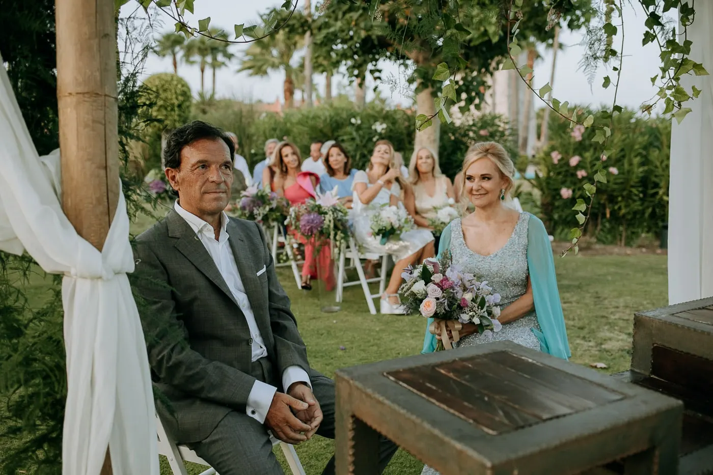 Bride and groom seated at the ceremony, guests behind
