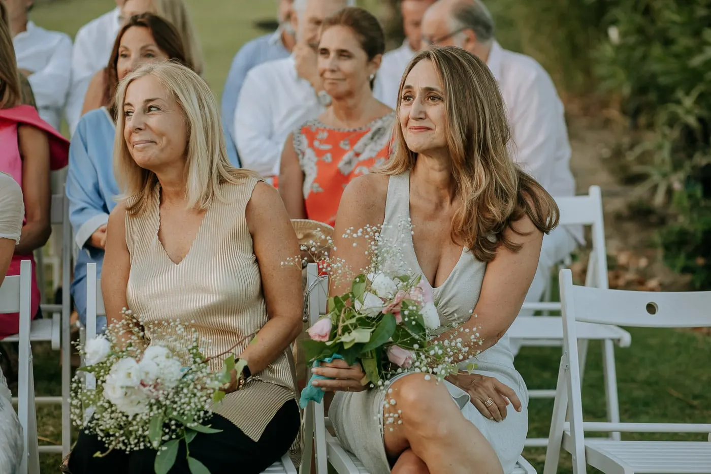 Two friends with bouquets smiling during the ceremony