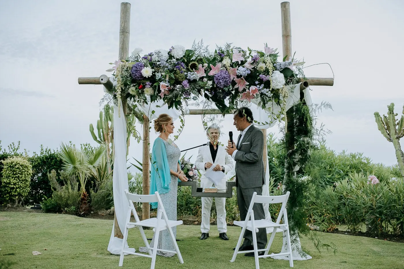 Bride, groom and officiant under the flower arch, Tikitano