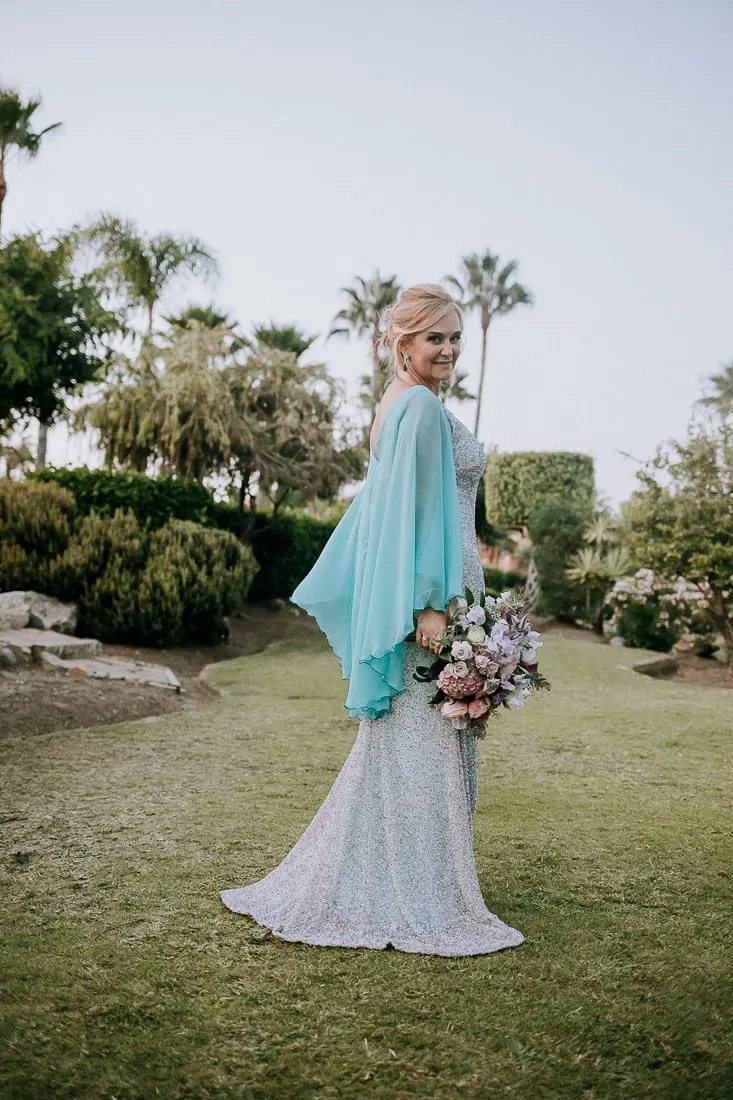 Bride in her silver gown and turquoise cape on the lawn