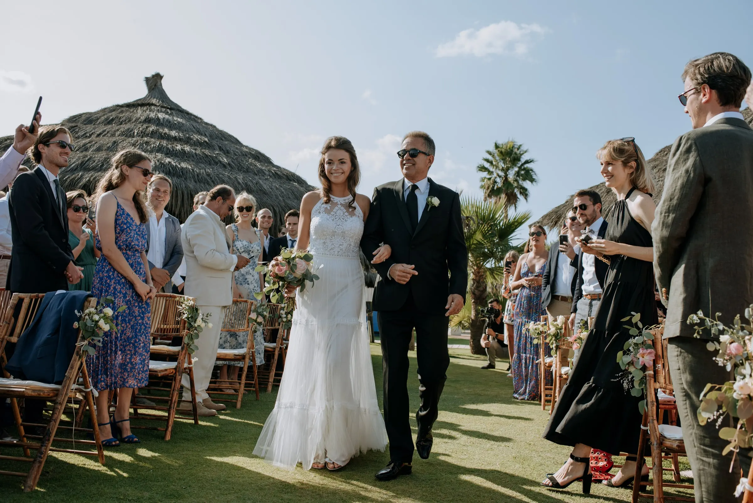 Bride walking down the aisle on her father's arm between smiling guests, Trocadero, Sotogrande